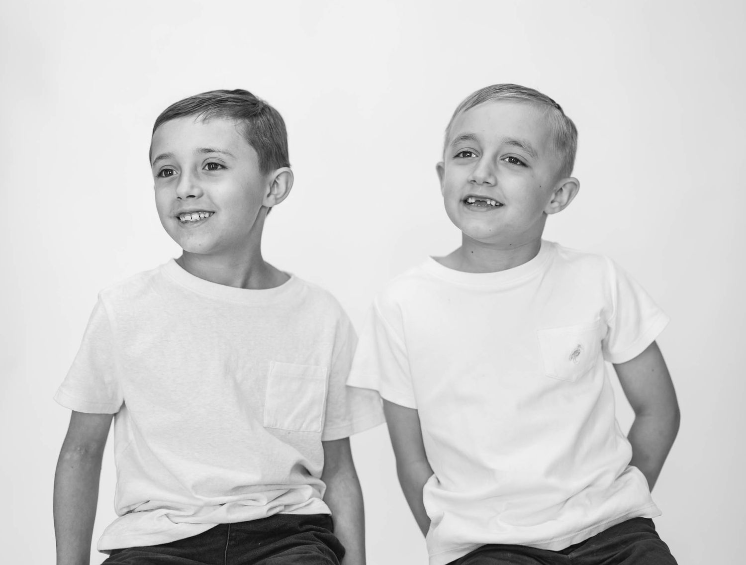 Two young boys in white t-shirts smiling in a black and white portrait photo.