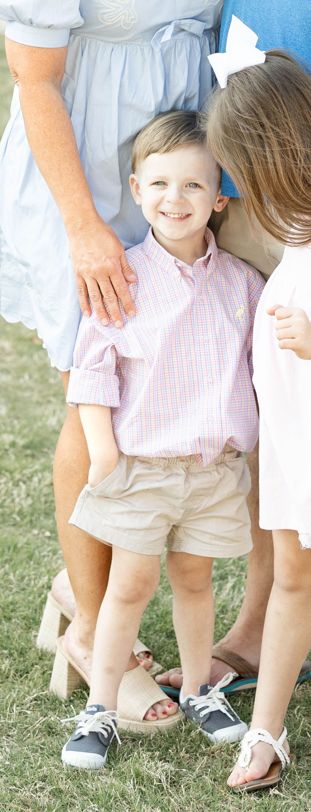 Adorable smiling young boy in a pink plaid shirt and khaki shorts standing with his family.