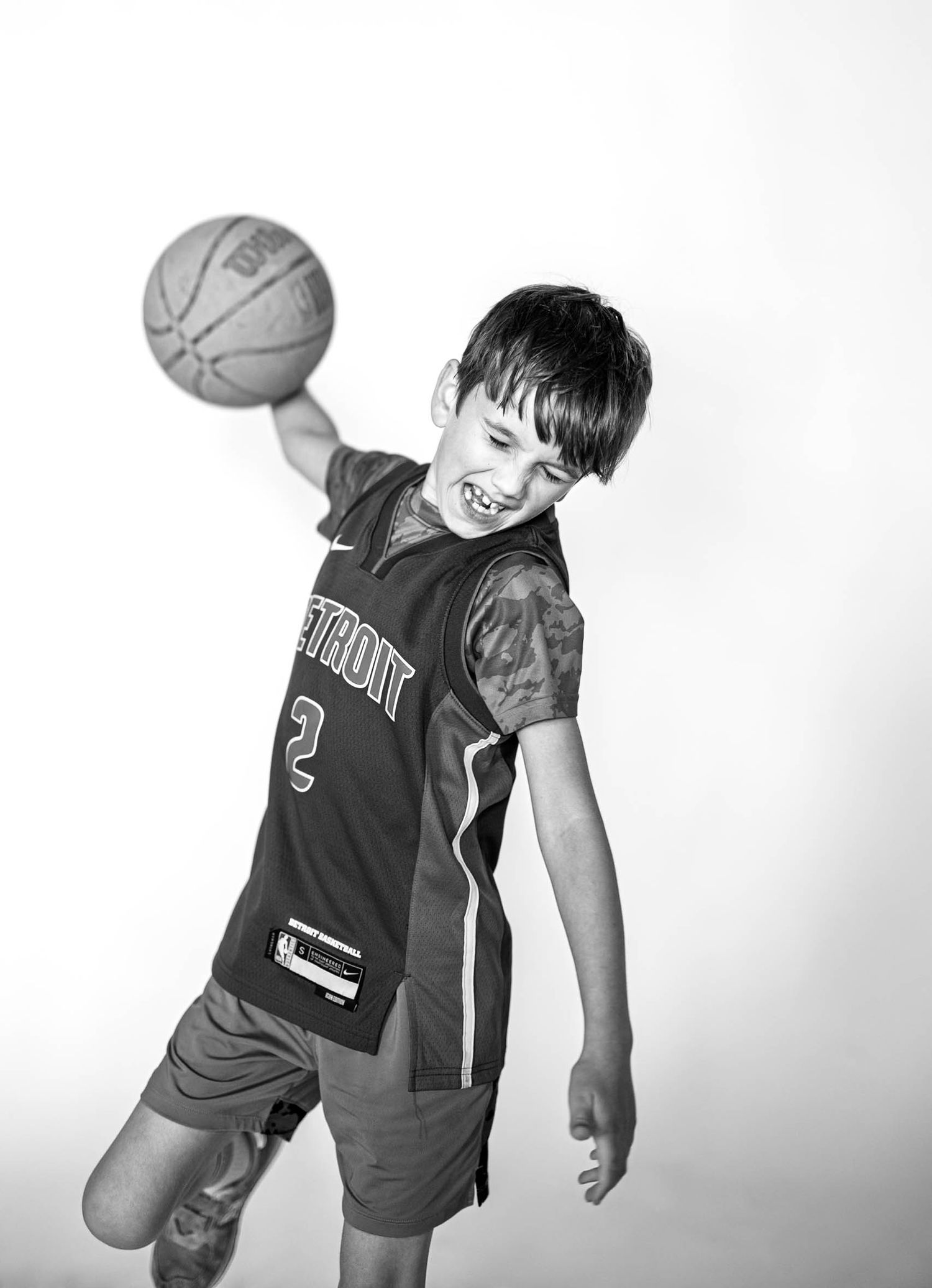 Boy in Detroit #2 jersey spinning basketball on finger, black and white photo.