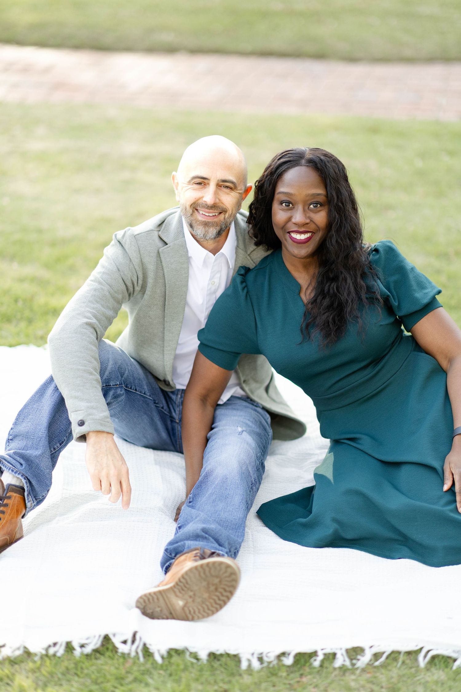 Happy interracial couple sitting together on a white blanket on a green grassy lawn outdoors.