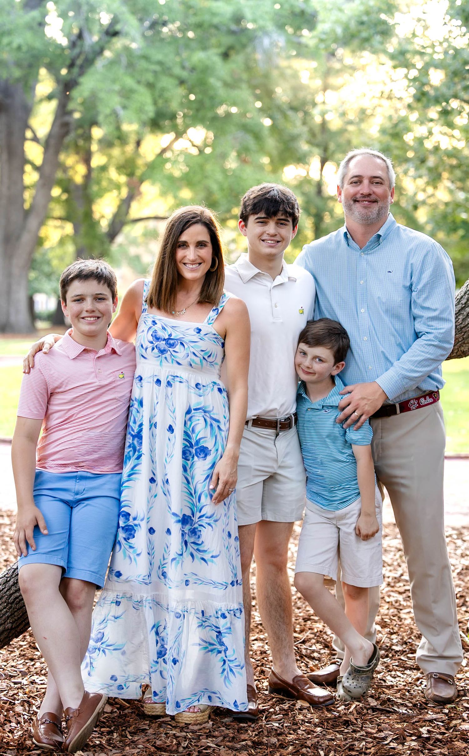 Happy family of five posing outdoors in a park, wearing coordinated pastel outfits for a professional family portrait.