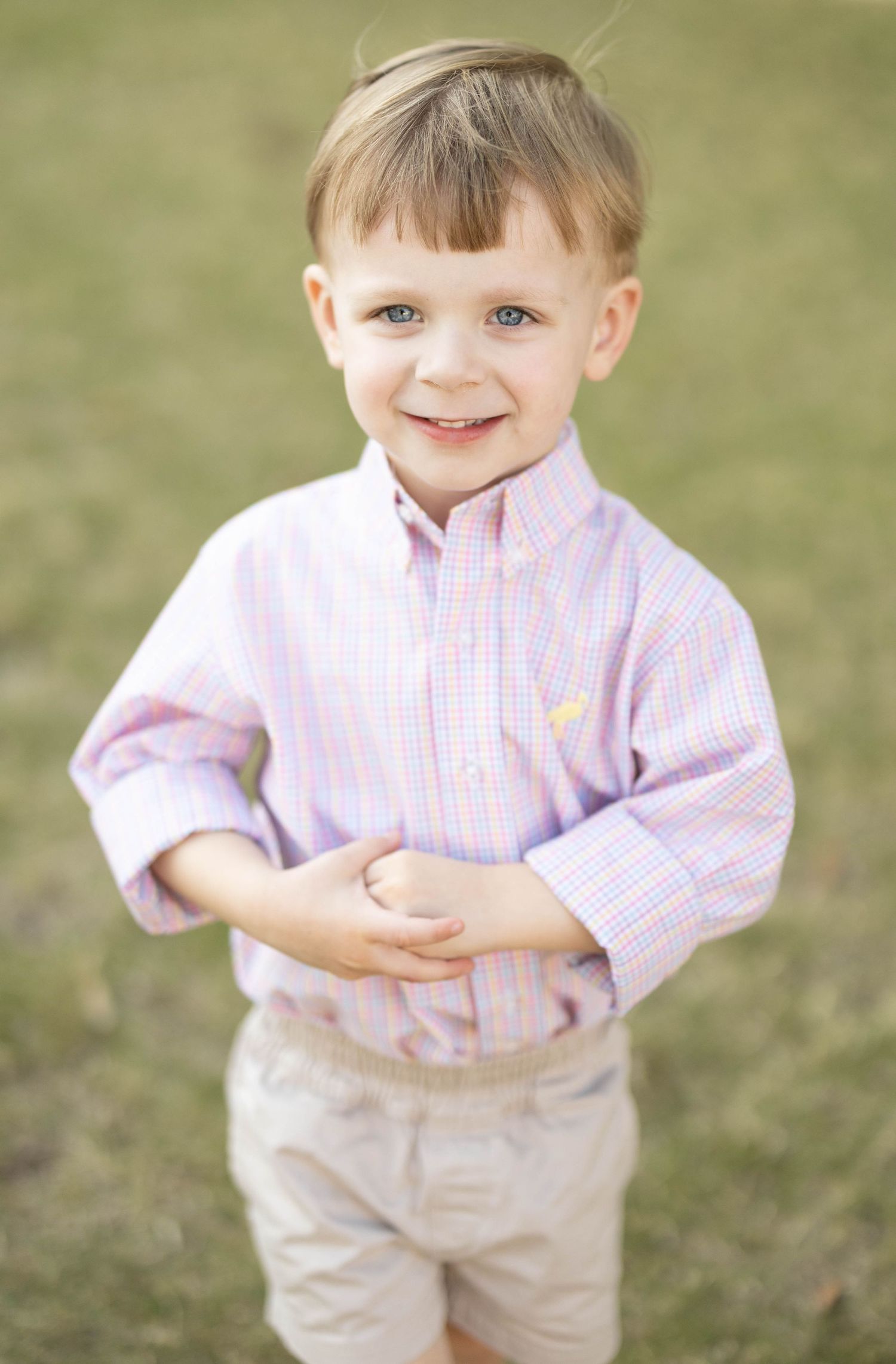 Adorable young boy in pink plaid Ralph Lauren button-down shirt smiles outdoors.
