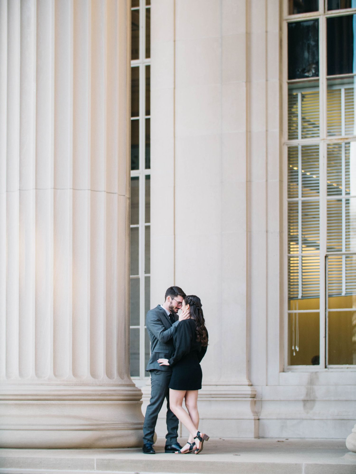 Couple sharing a kiss on steps between tall white columns of a neoclassical building.