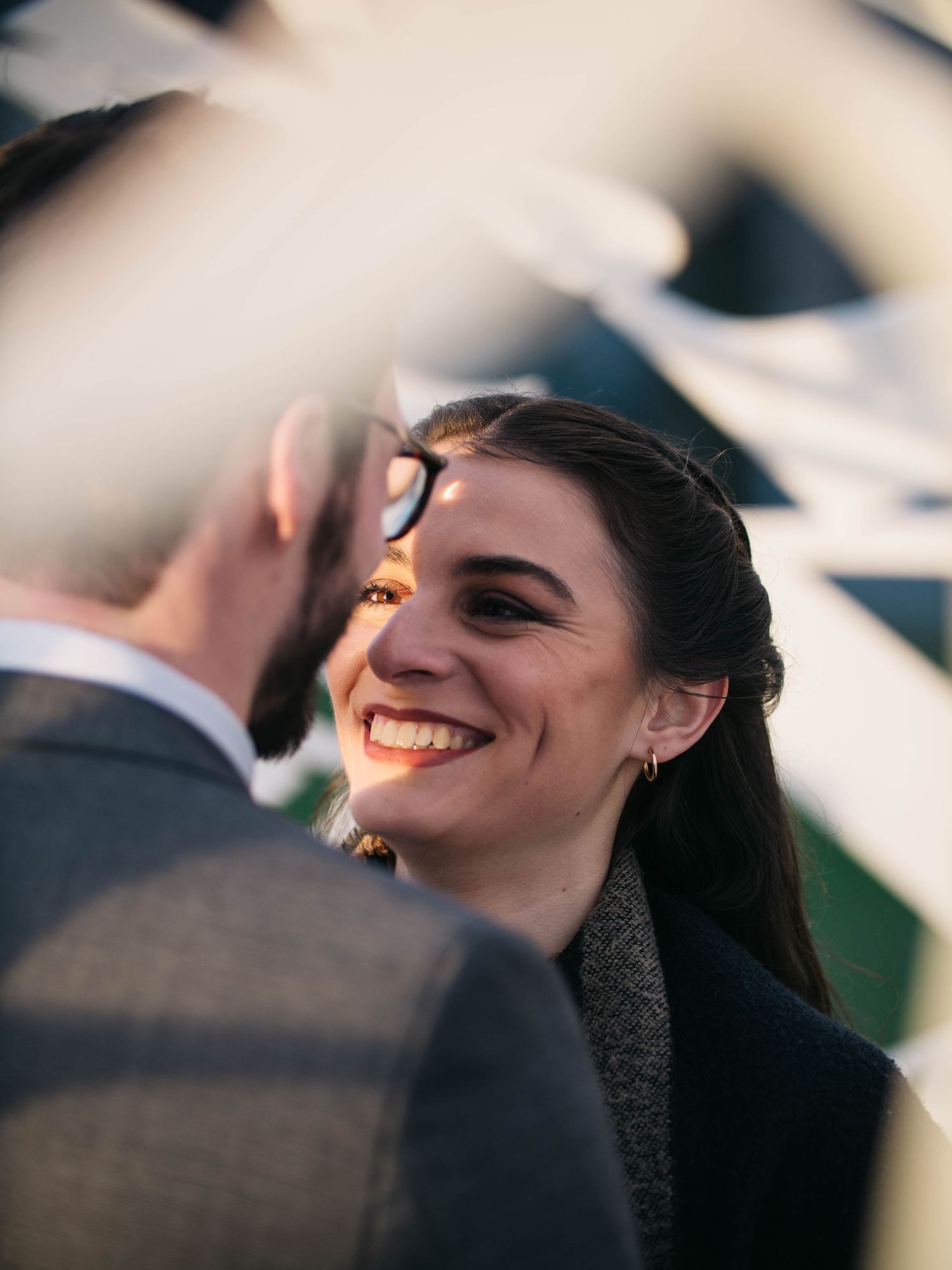 Smiling brunette woman gazing lovingly at her partner during golden hour engagement session.