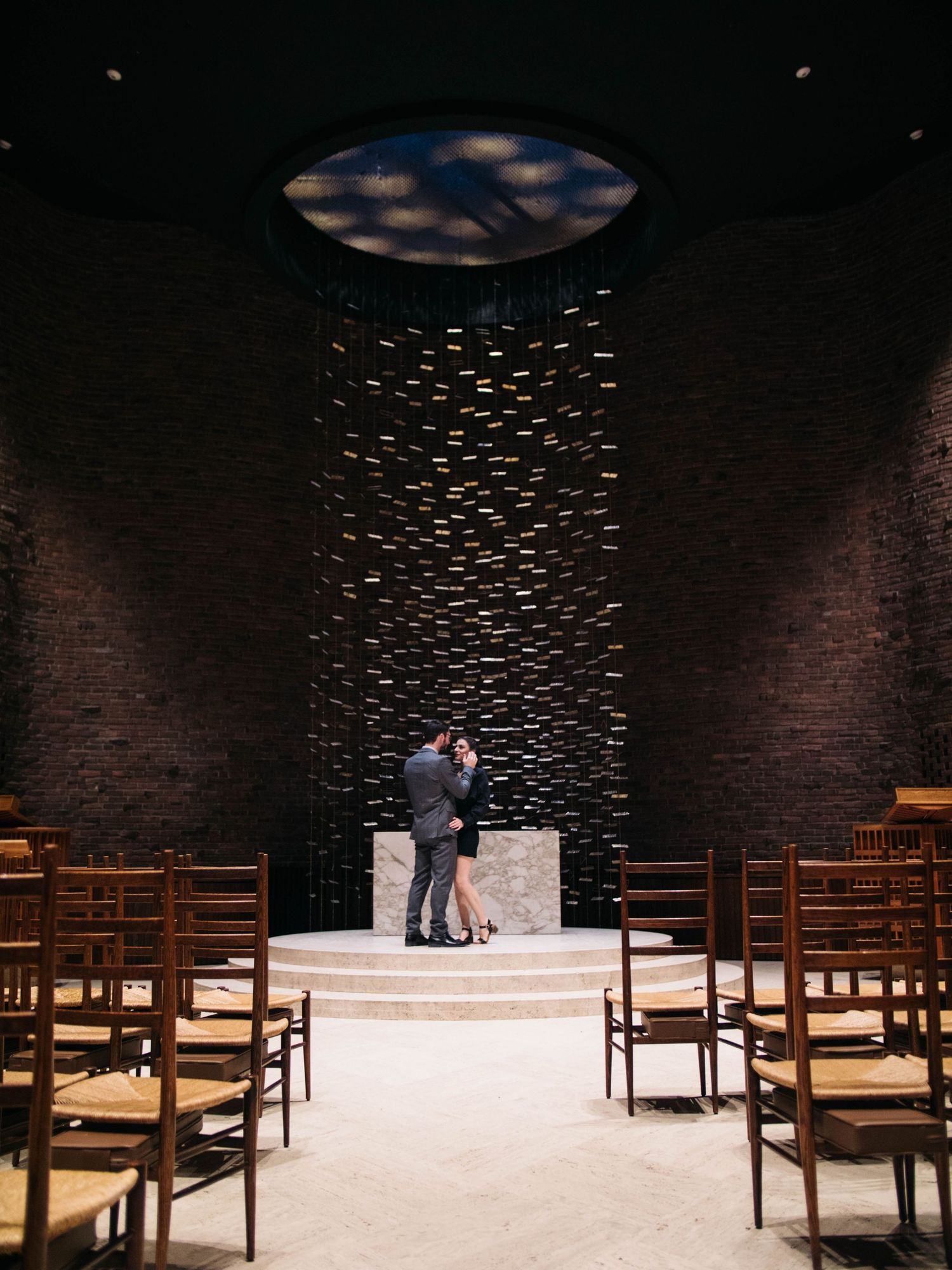 Couple embracing at altar inside a dramatic dark chapel with decorative ceiling installation.