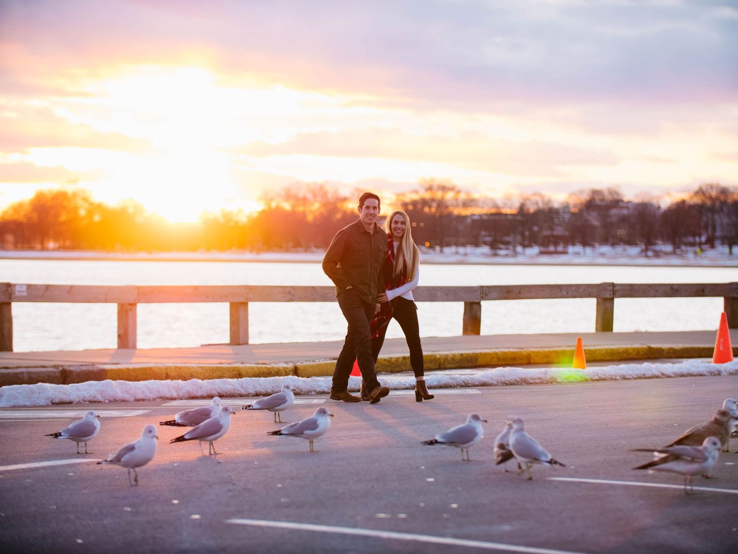Couple posing at sunset near a waterfront with seagulls in the foreground.