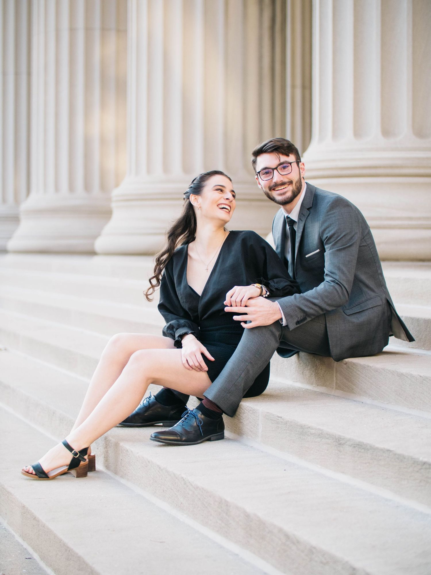 Smiling couple in formal attire sitting on steps of a building with large columns.