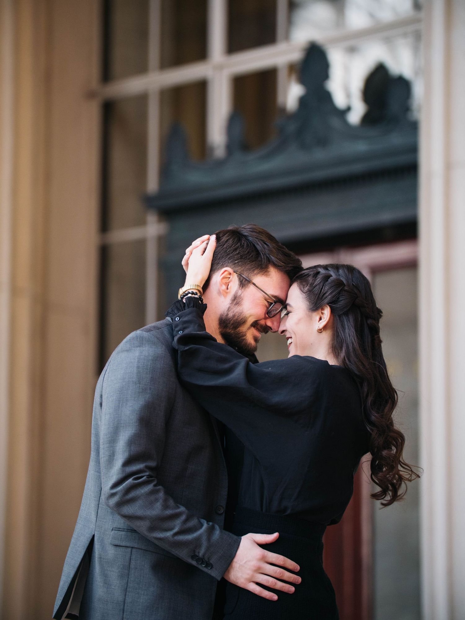 Couple embracing and smiling at each other in front of an ornate building entrance.