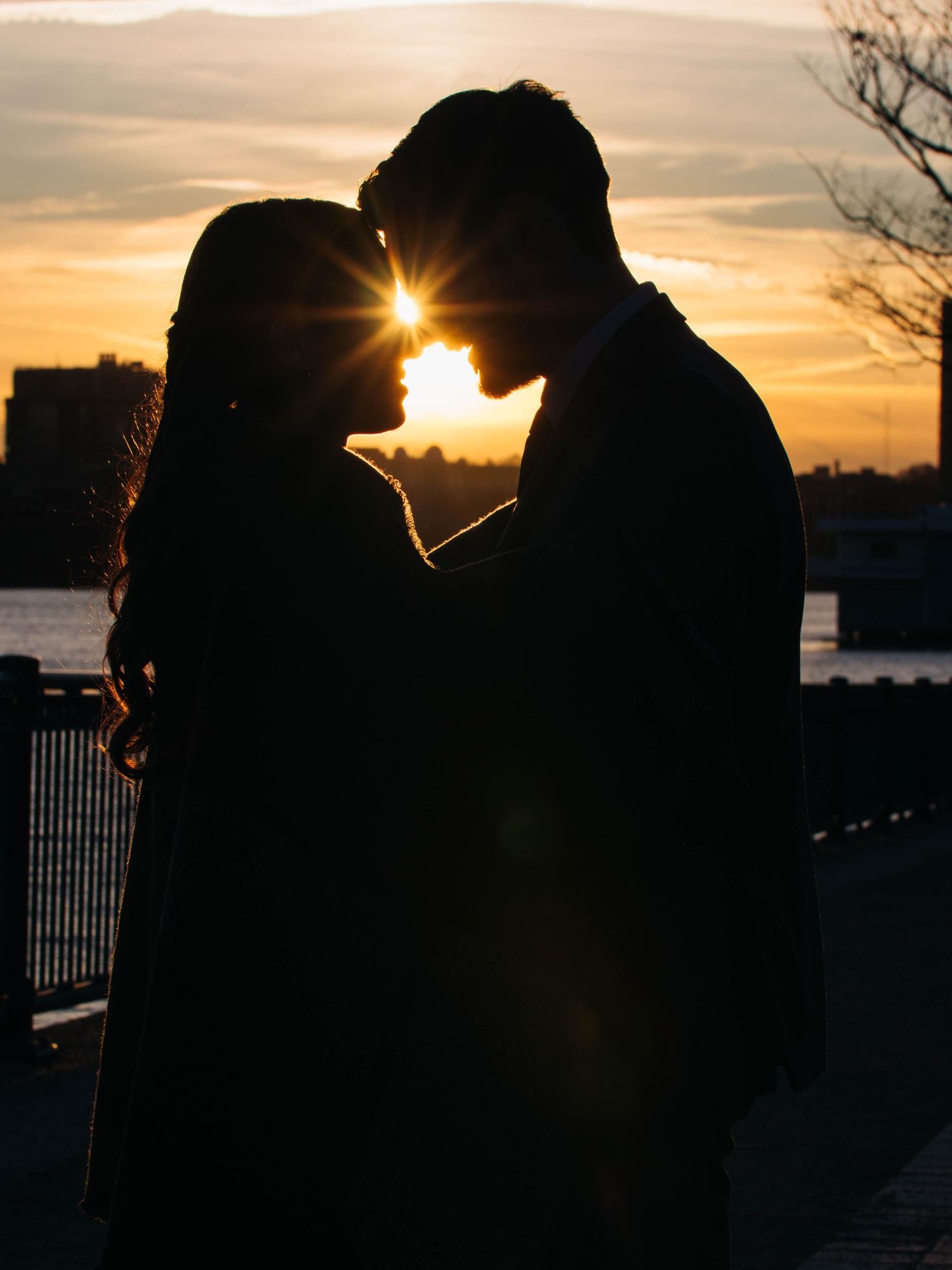 Romantic silhouette of couple nearly kissing with golden sunset and river in the background.