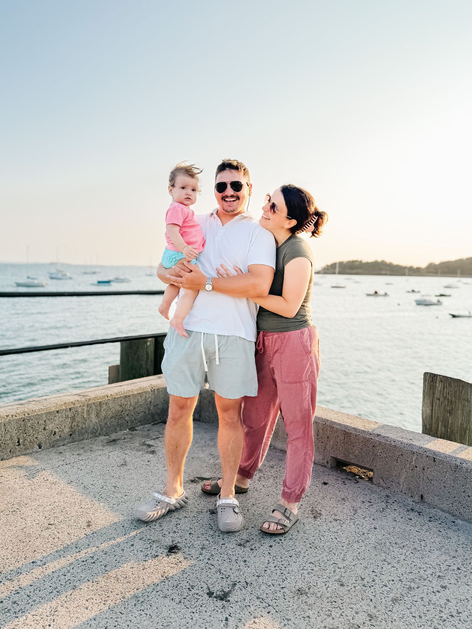 A happy family with a baby poses on a waterfront pier during a golden sunset.