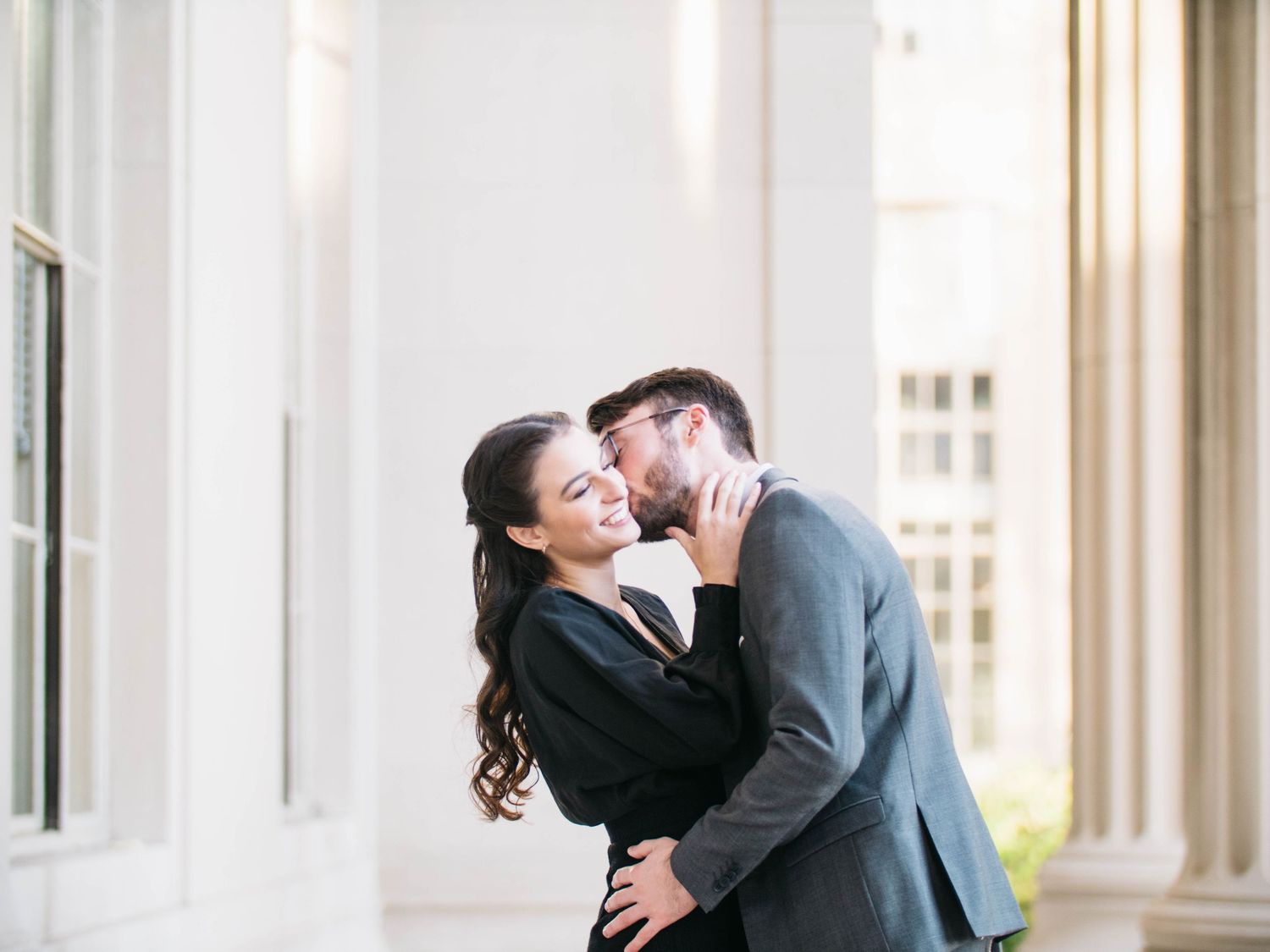 Couple sharing a romantic kiss between white columns of a grand building.