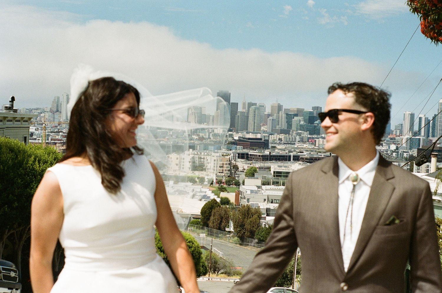 Bride and groom smile outdoors with San Francisco skyline backdrop on their wedding day.