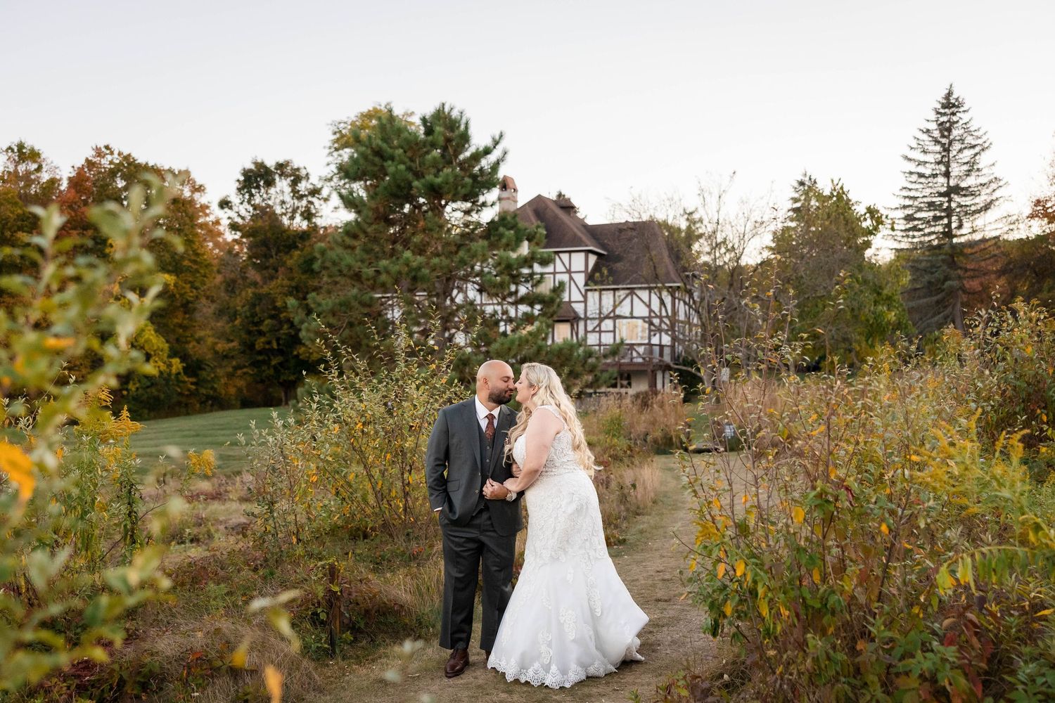A wedding couple walks through a lush garden path surrounded by vibrant fall foliage on their special day.