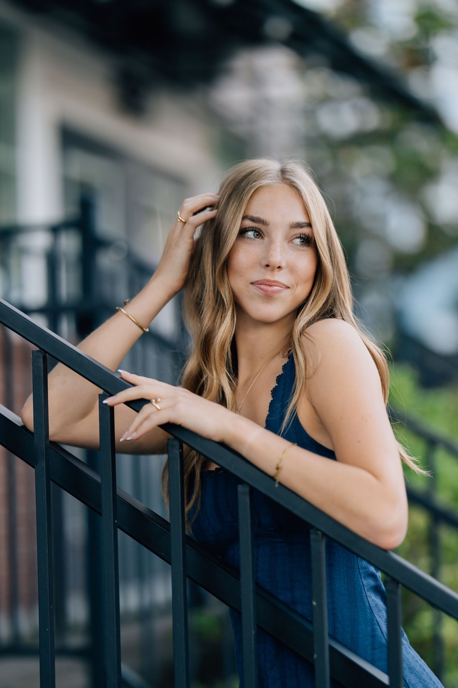 Tri-Cities senior photographer. Young blonde woman in blue dress leans on black iron railing outdoors in a candid portrait photo.