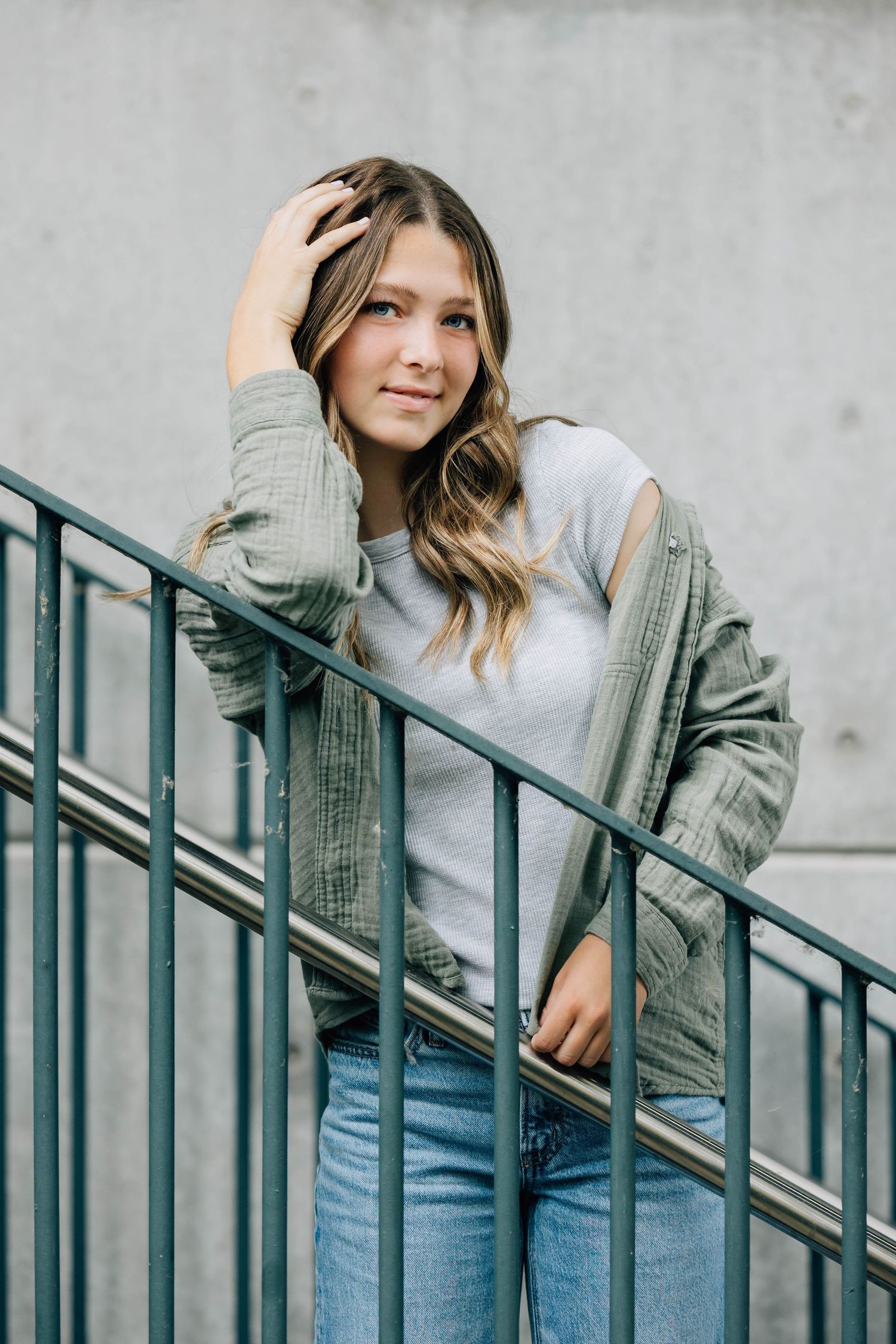 Young woman in green jacket and jeans posing on staircase railing.