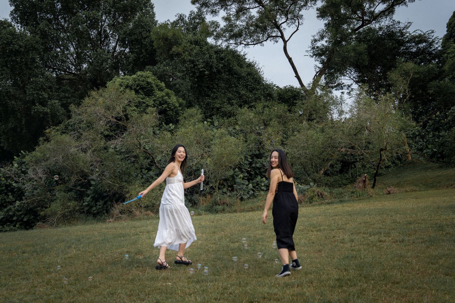 Two people dance joyfully together in a grassy meadow surrounded by trees on a summer day.