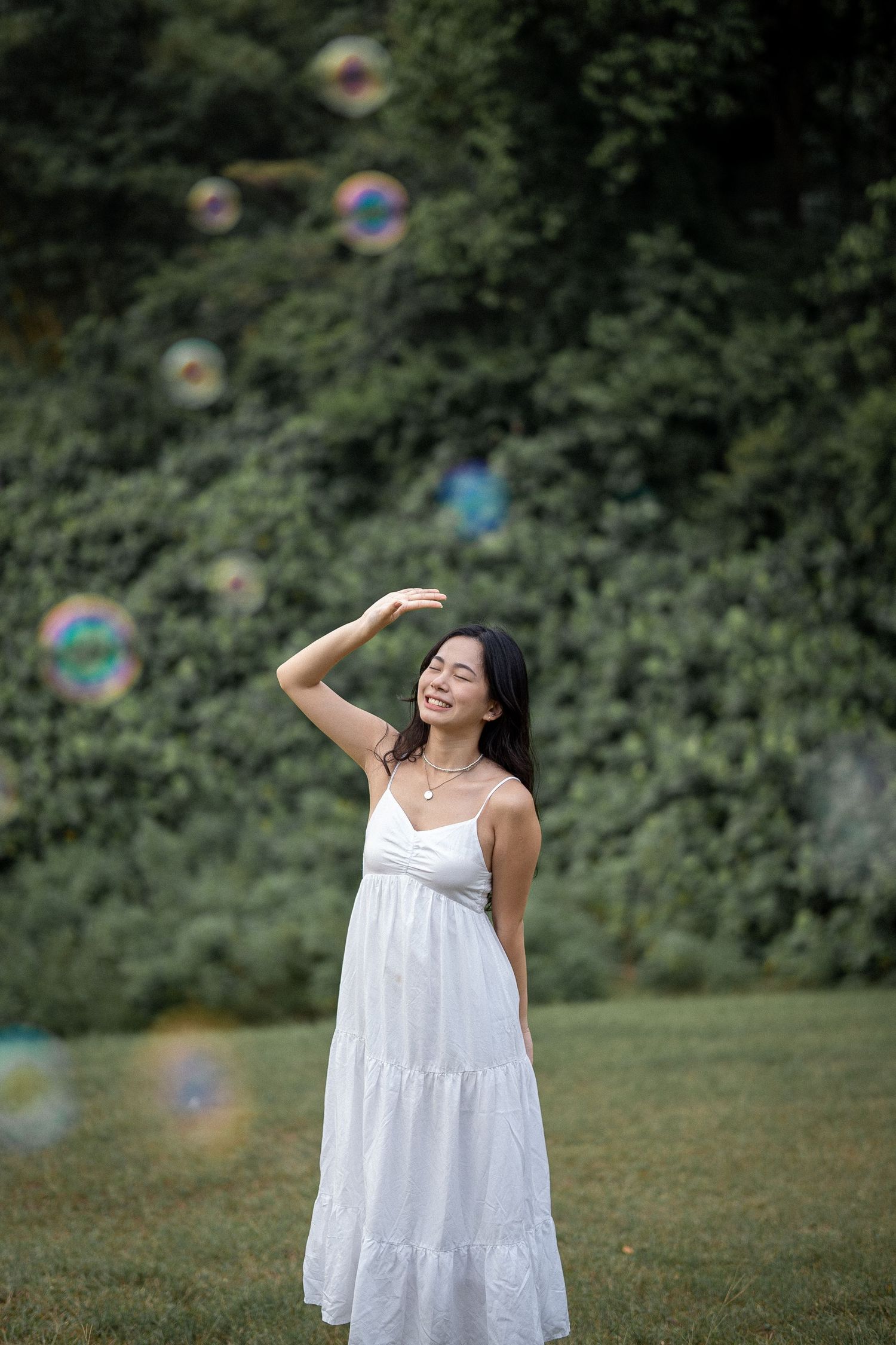 A white summer dress against lush greenery with floating soap bubbles in the background.