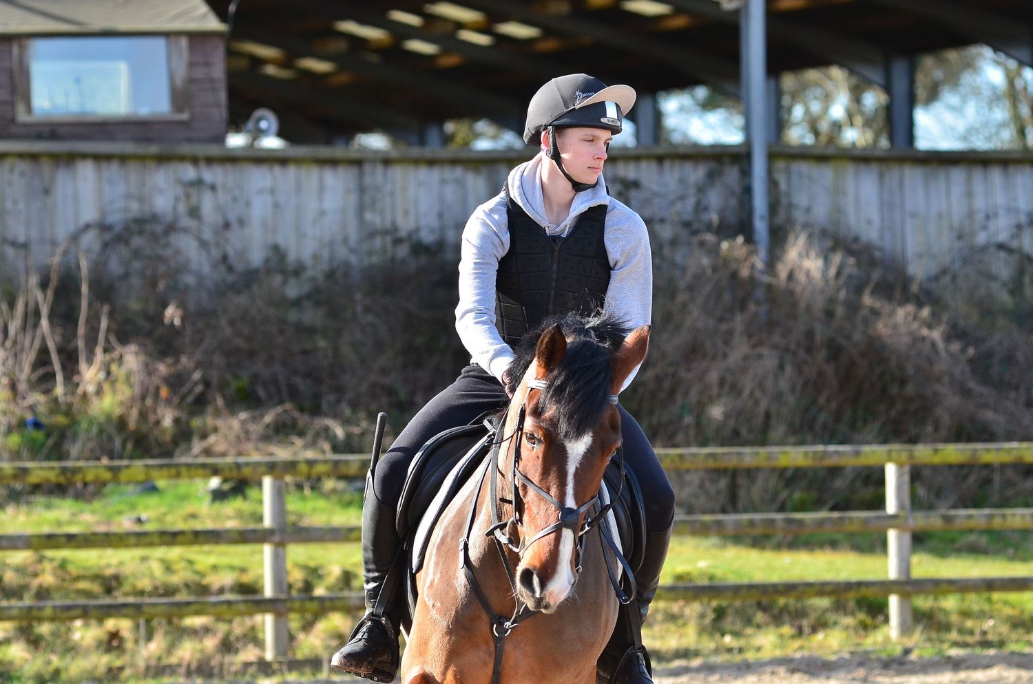 A rider in protective gear practices horseback riding in an indoor arena.