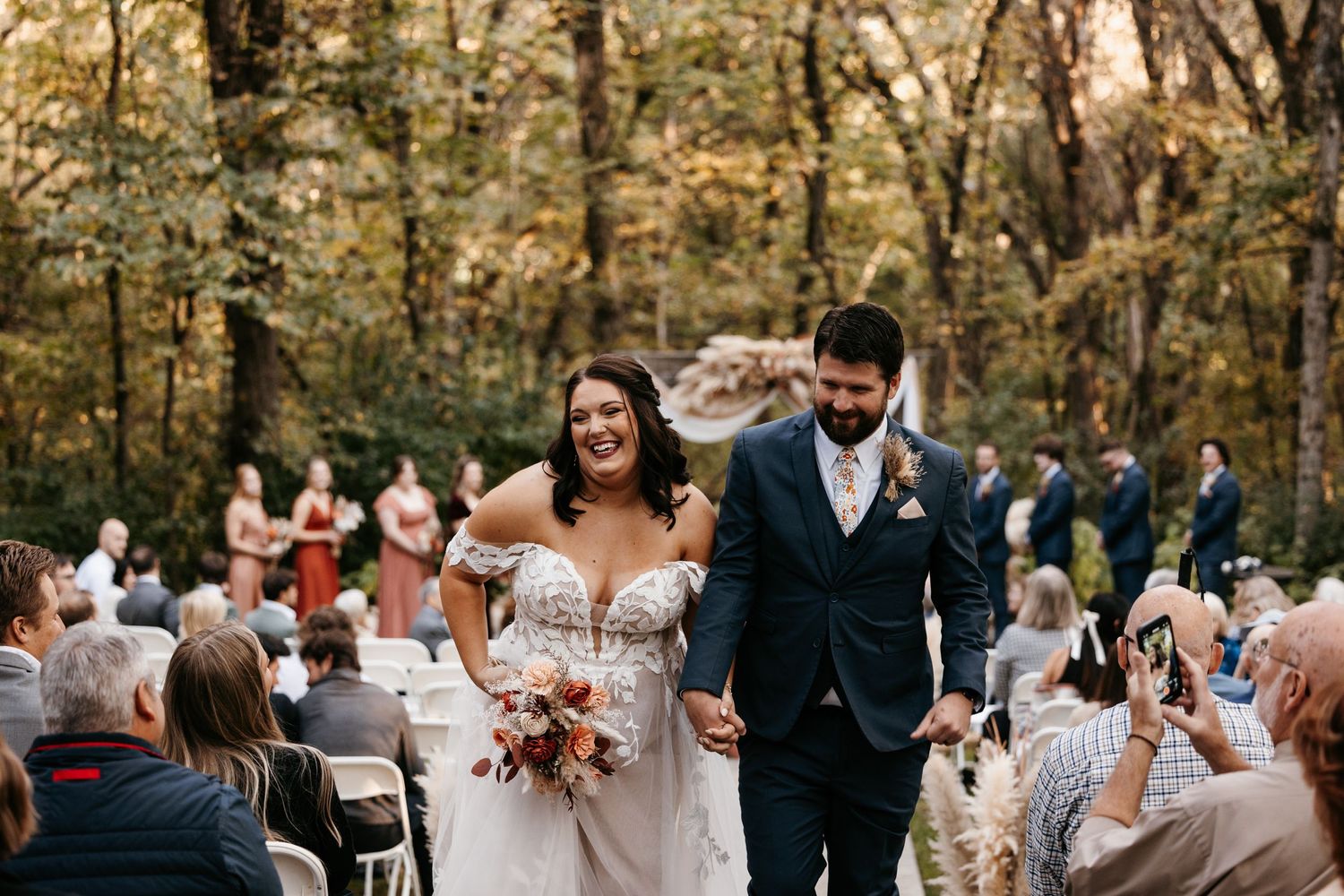 Wedding ceremony recessional in a beautiful autumn forest setting with guests cheering.