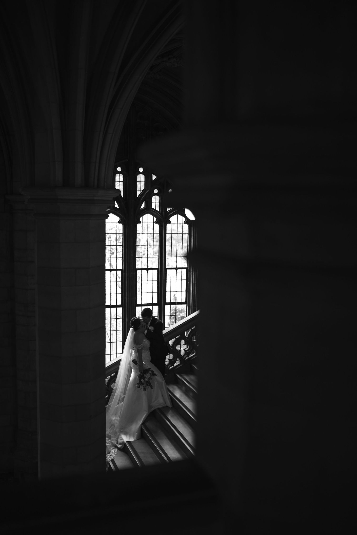 A dramatic black and white photograph captured through an arched church window with ornate gothic architecture.