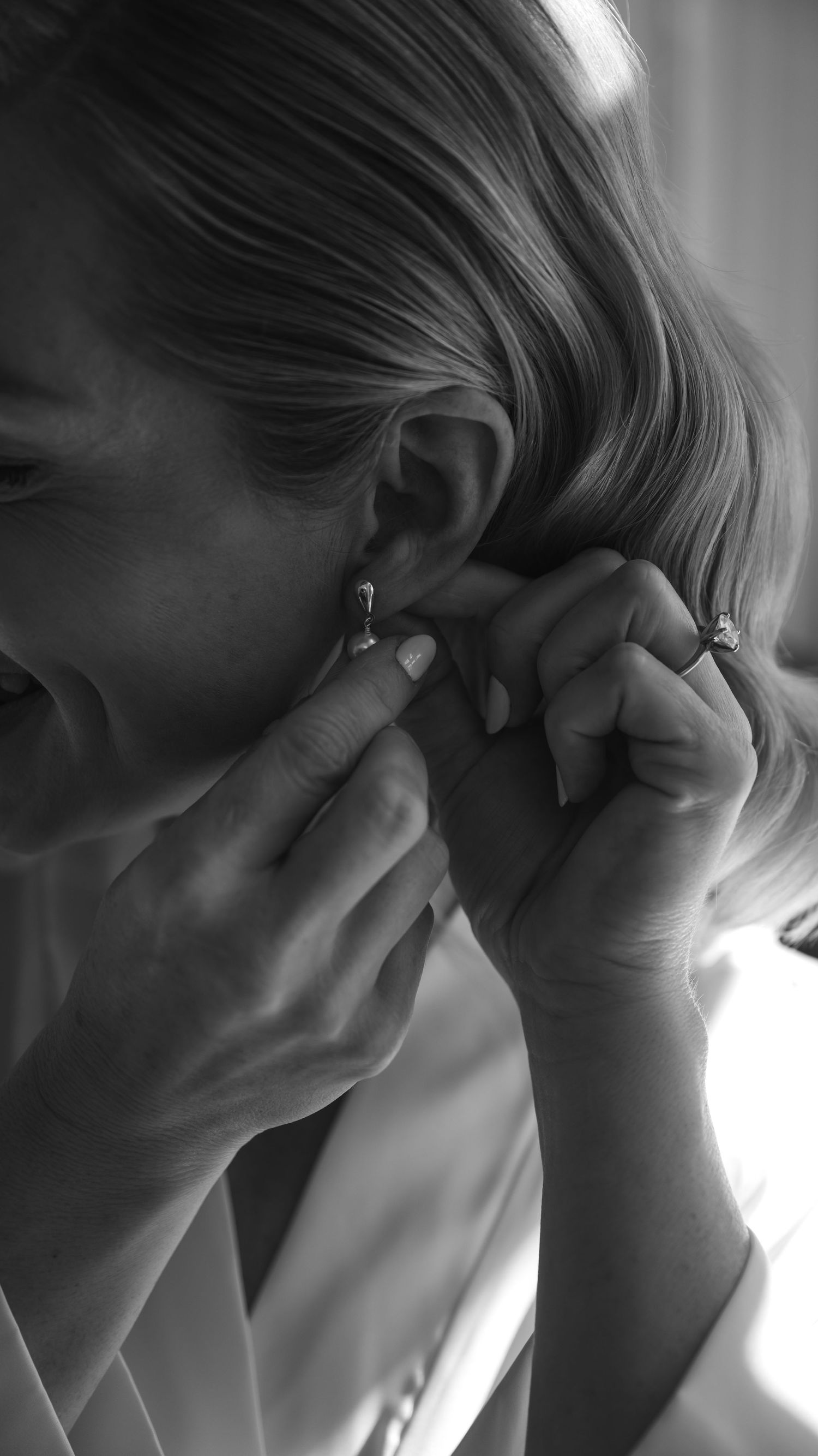 Close-up black and white photo of someone putting on earrings while getting ready.