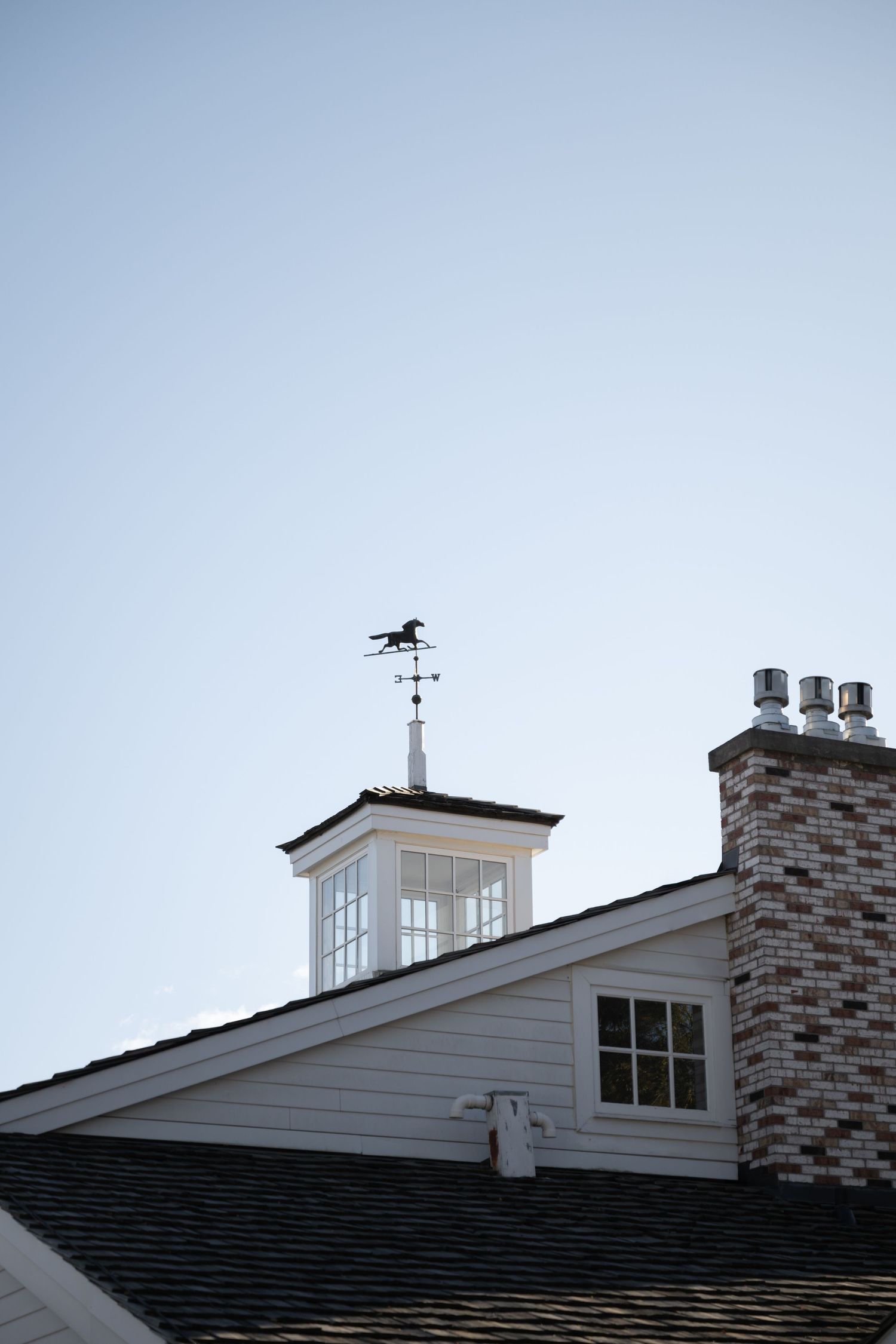 White cupola with weathervane on top of residential house against clear blue sky.