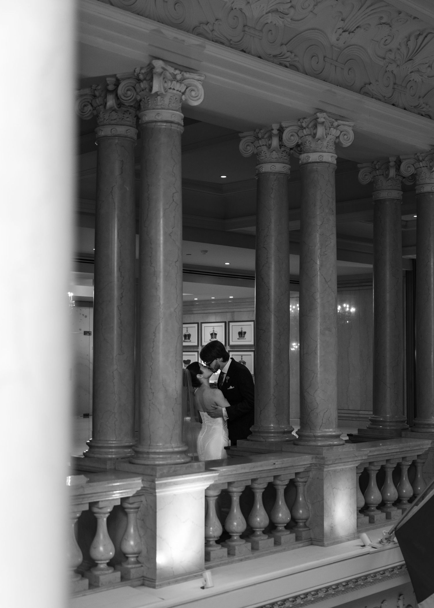 Couple sharing romantic moment between elegant marble columns in a grand ballroom venue.