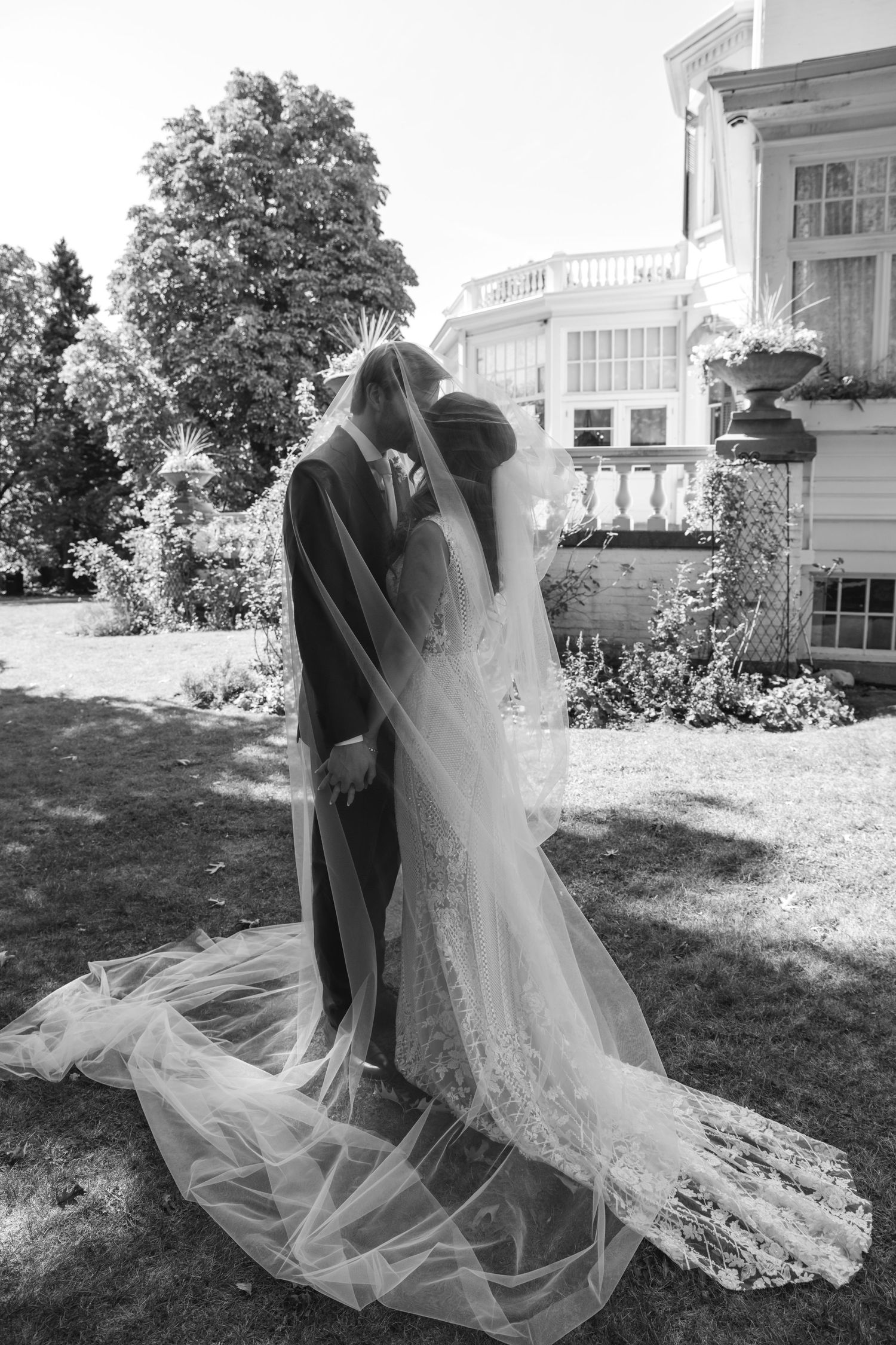 A couple shares a romantic moment in a garden setting on their wedding day under a long flowing veil.