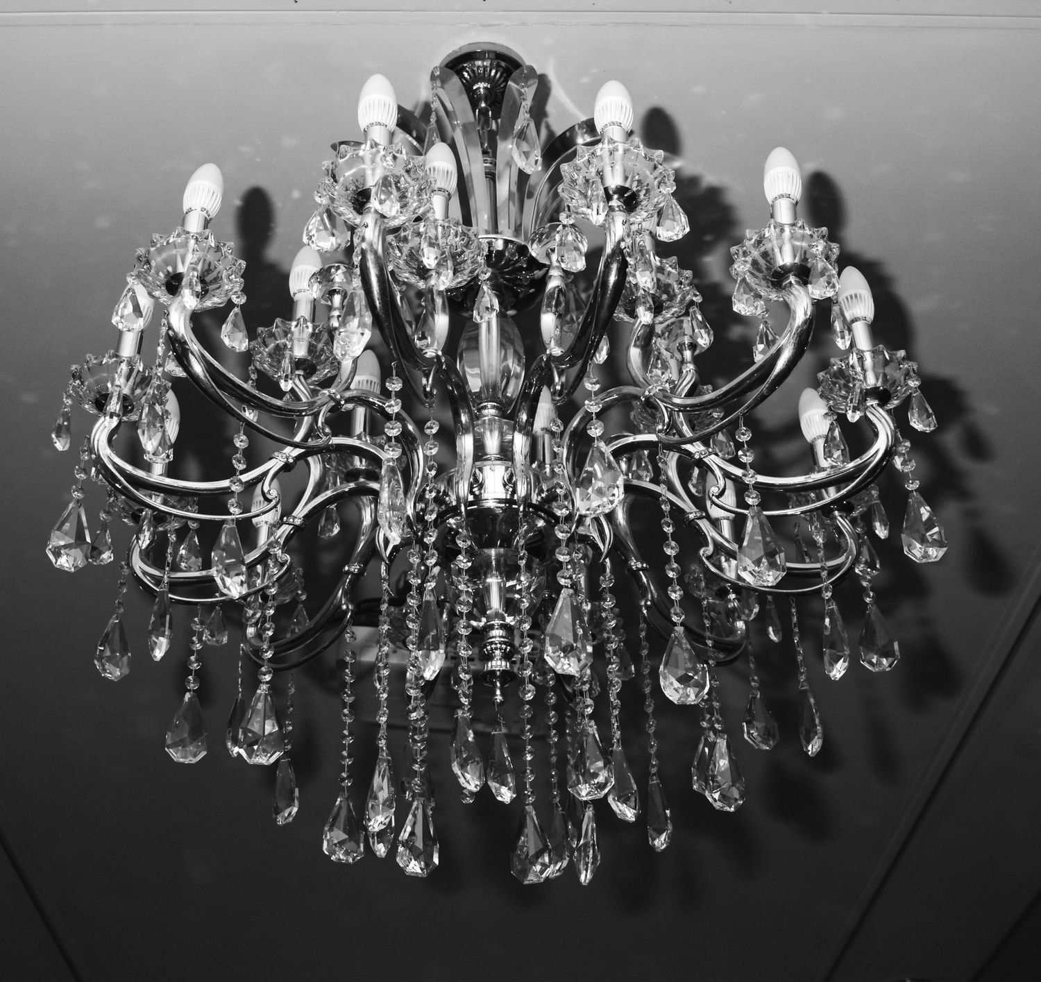 An elegant crystal chandelier with multiple tiers of hanging glass droplets photographed in black and white.