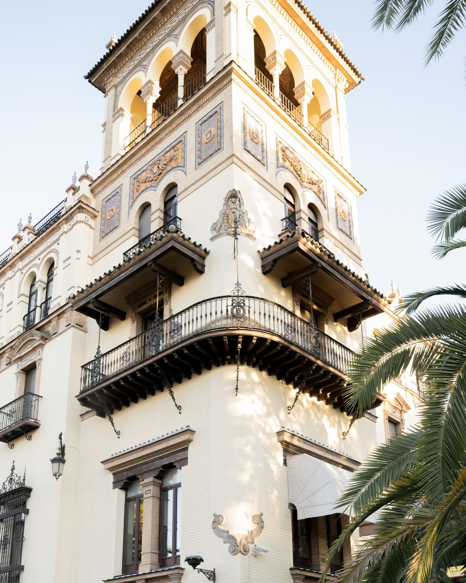Mediterranean style building with ornate balconies and palm trees in warm sunlight.