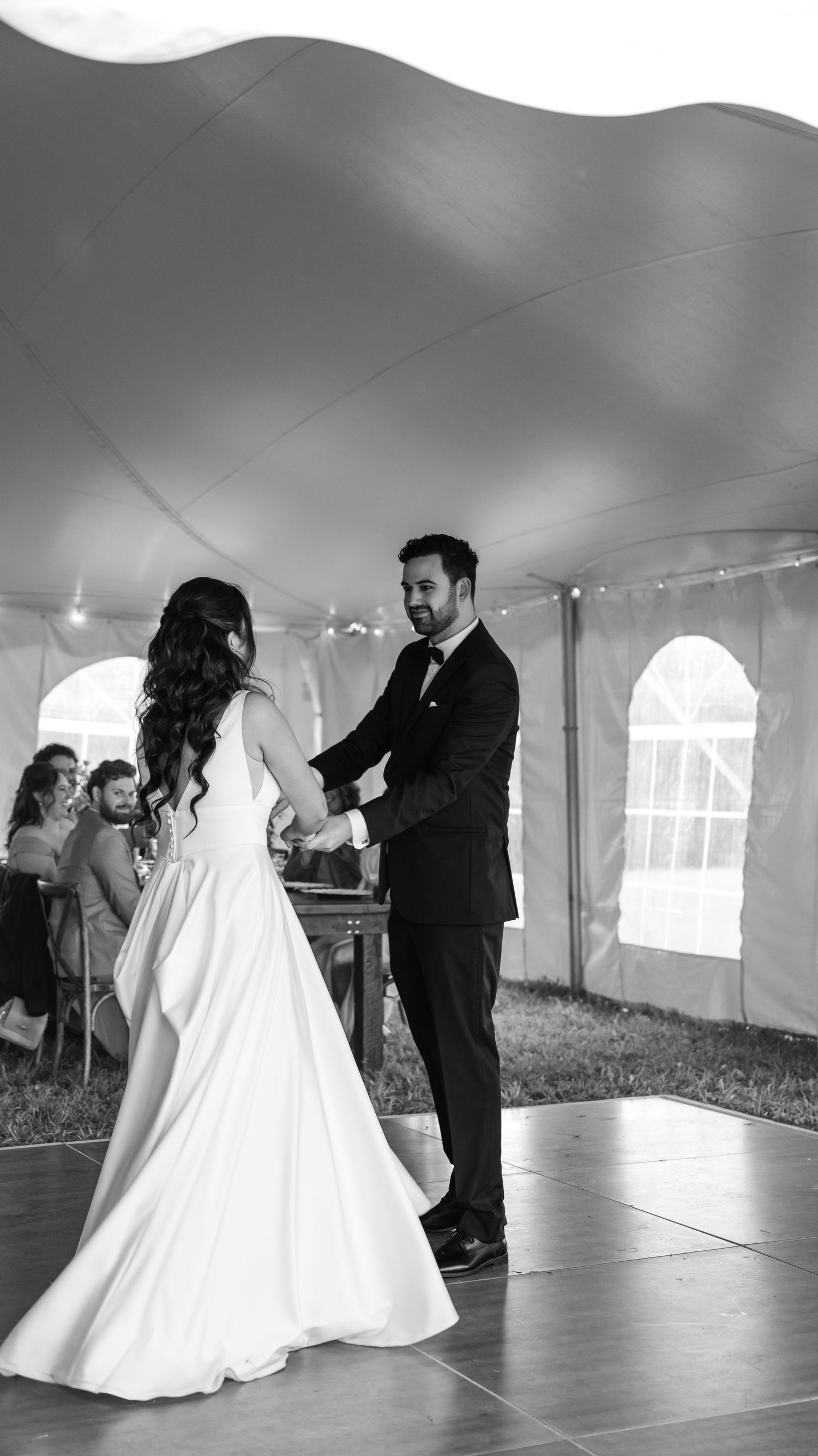 A couple shares their first dance at their wedding reception under a white tent with a romantic atmosphere.