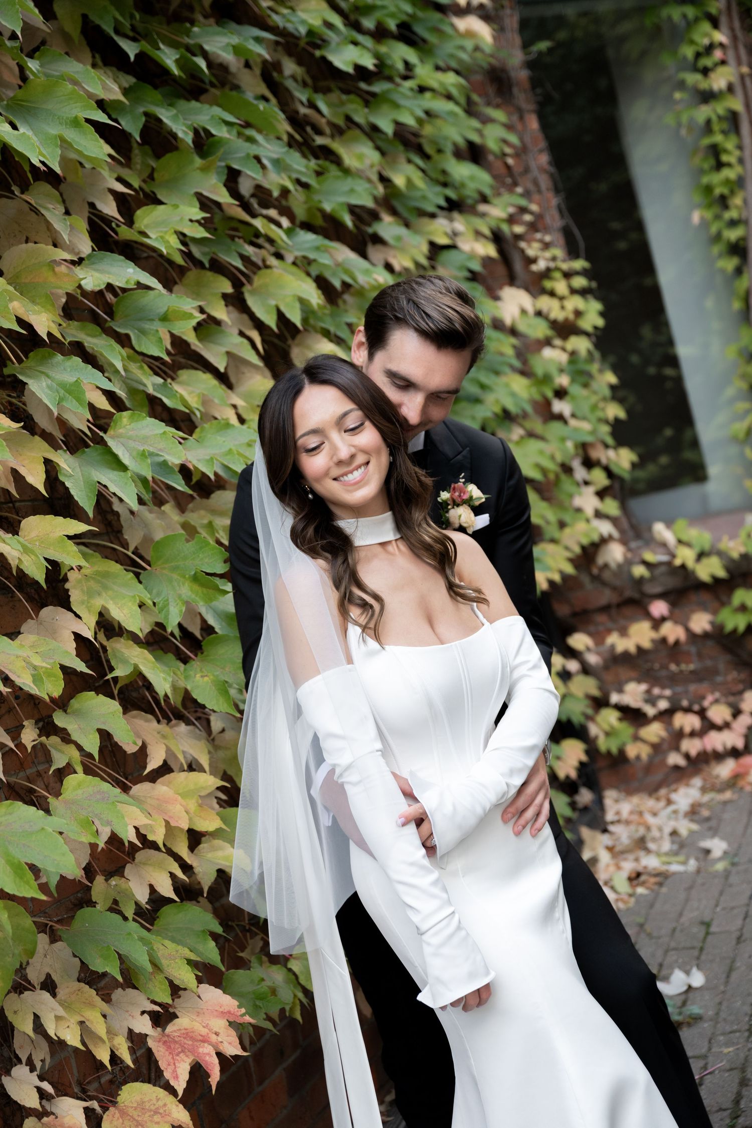 A romantic autumn wedding portrait with newlyweds embracing against a backdrop of colorful ivy-covered walls.
