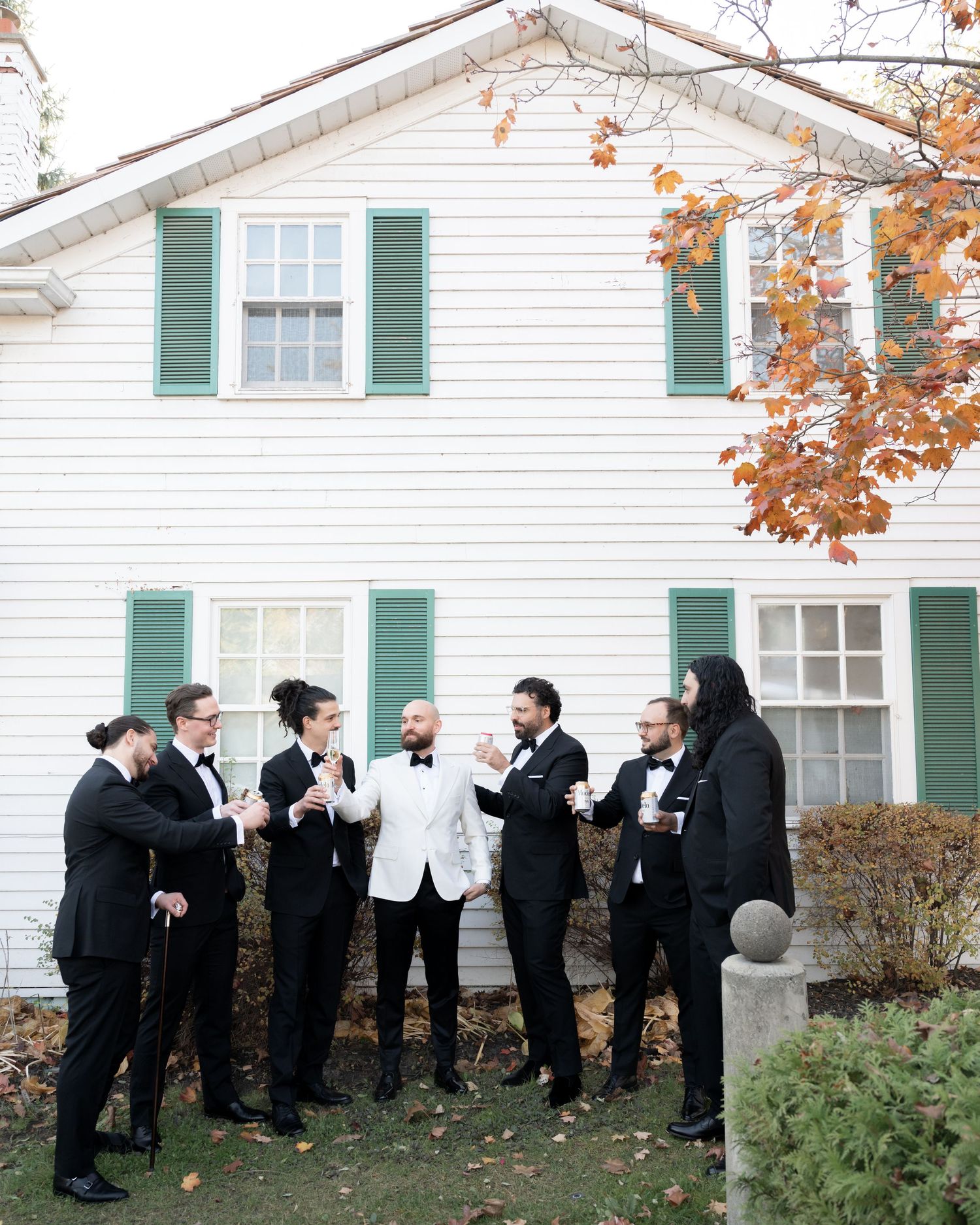 A group celebrating outside a white house with green shutters during fall.