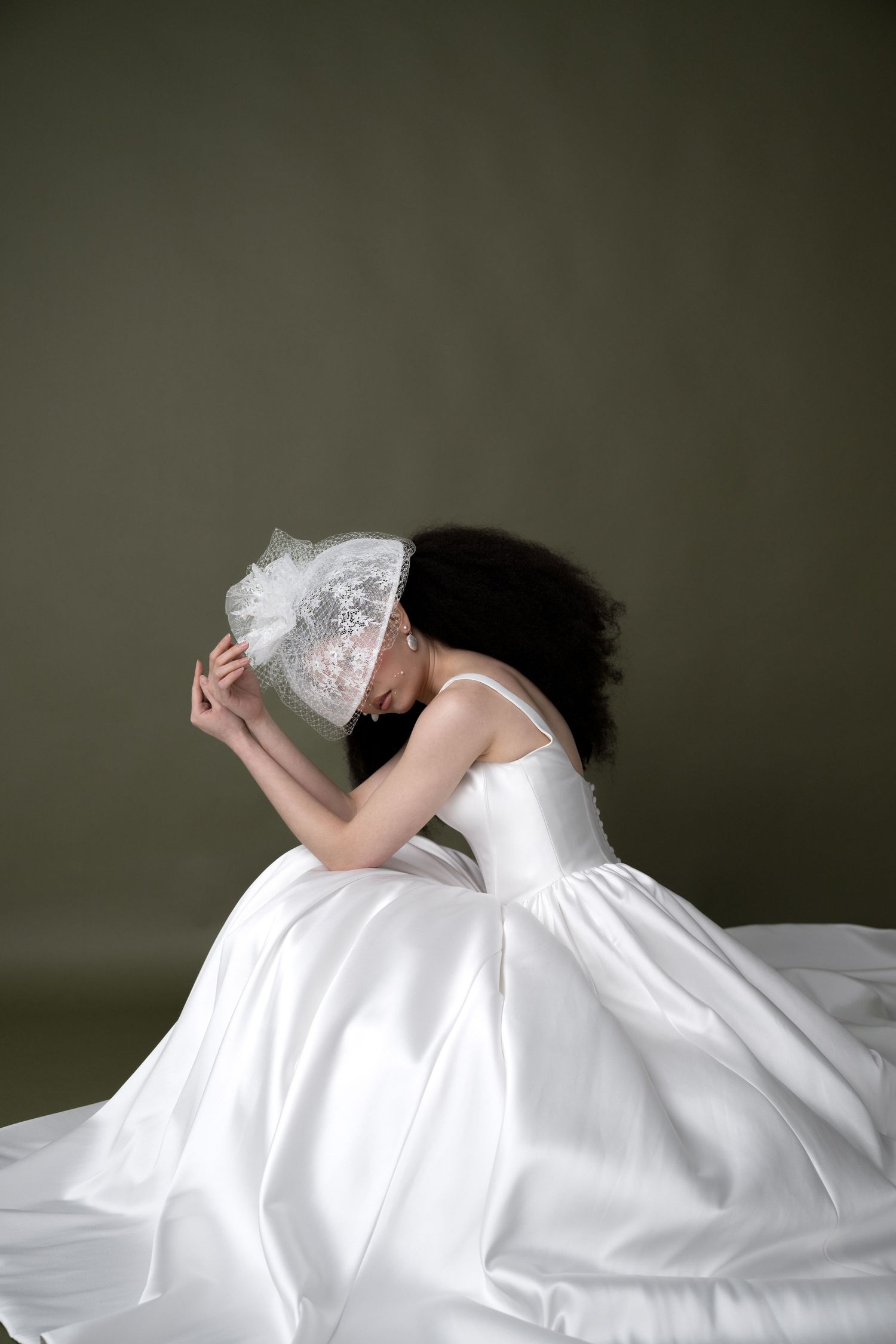 A graceful figure in a flowing white wedding gown and veil crouches down in an artistic pose against a dark backdrop.