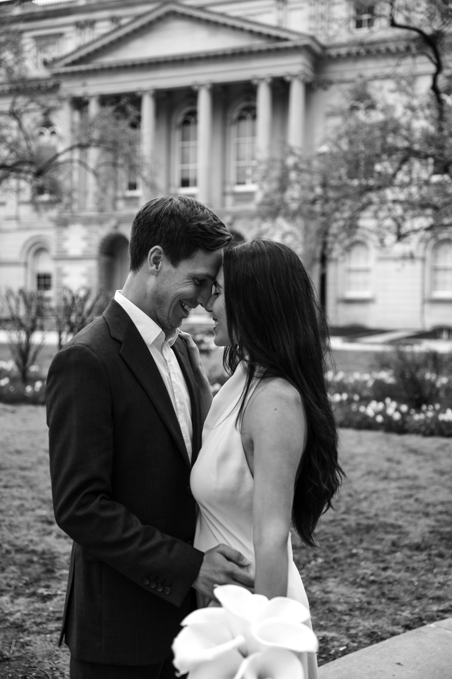 A romantic black and white photograph of a couple sharing an intimate moment outside a stately building with columns.