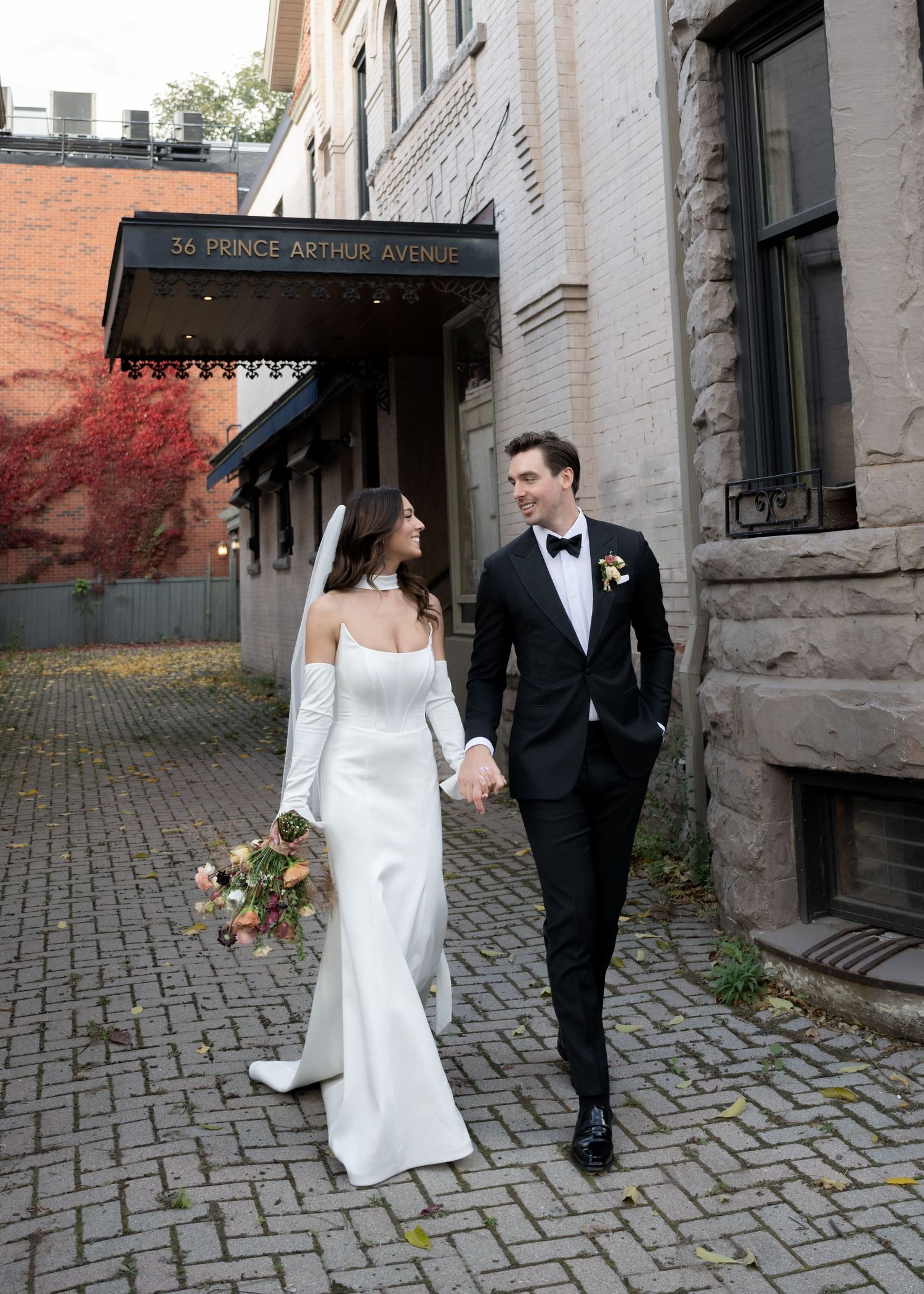 A couple walks together on cobblestone path wearing formal wedding attire.