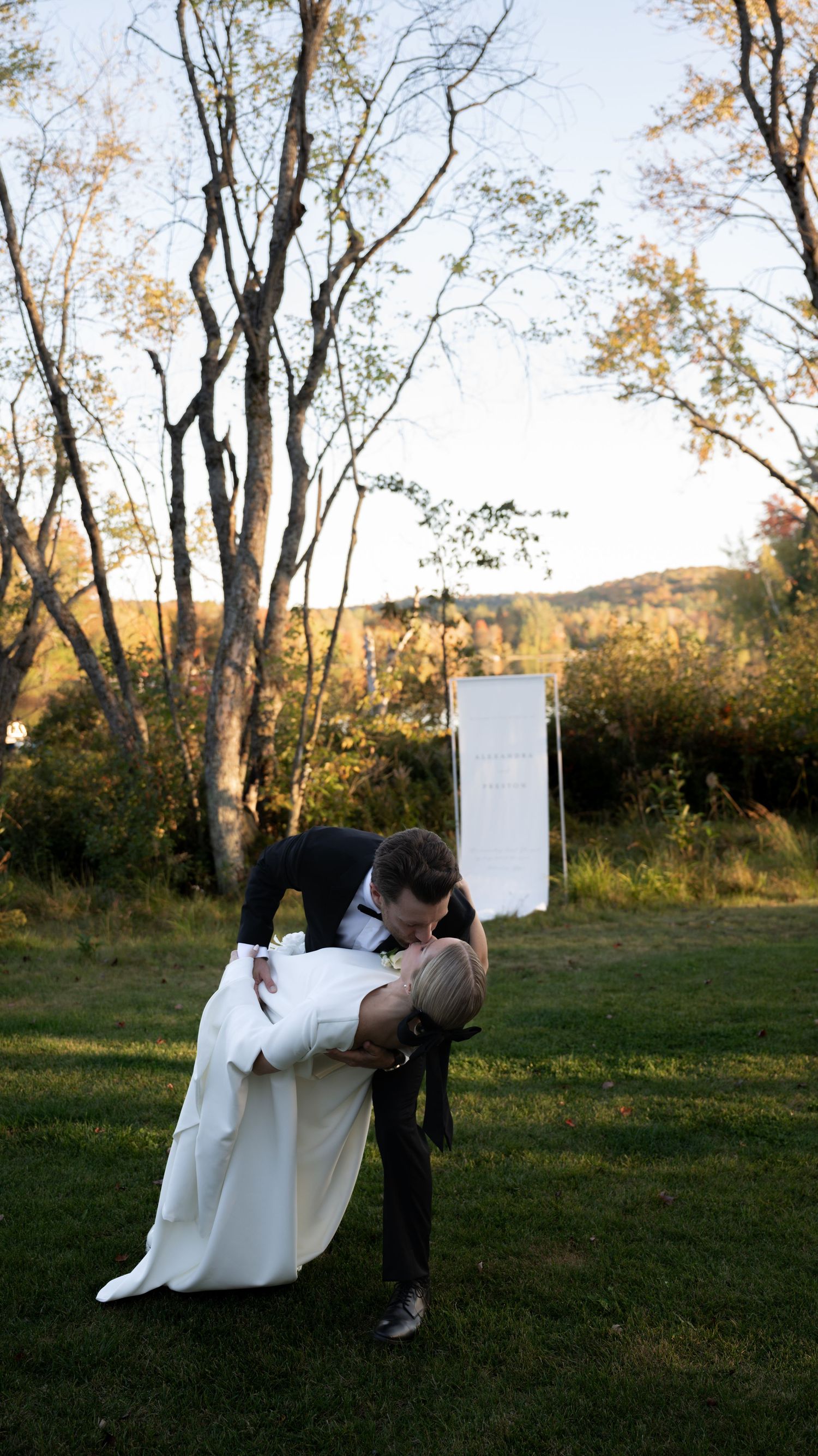 A romantic outdoor wedding scene with a dip kiss against a backdrop of autumn trees.