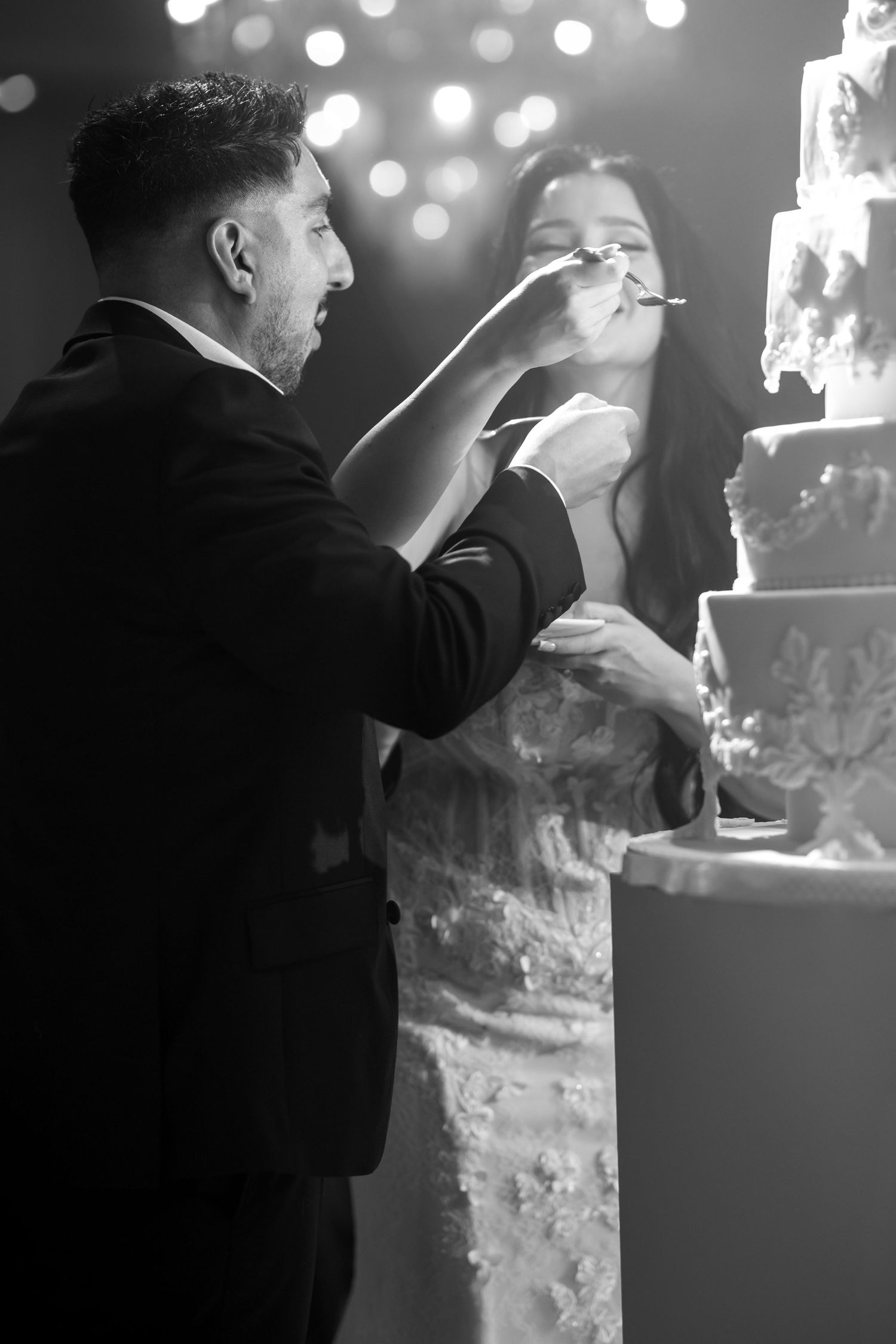 A couple shares a tender moment during their wedding cake cutting ceremony in black and white photography.