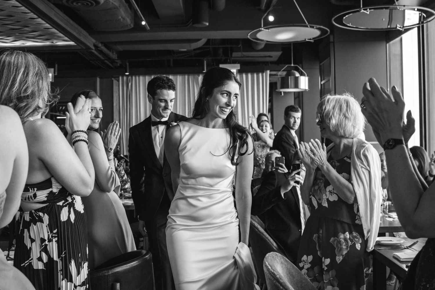 A black and white candid photograph of celebrating guests at a wedding reception.