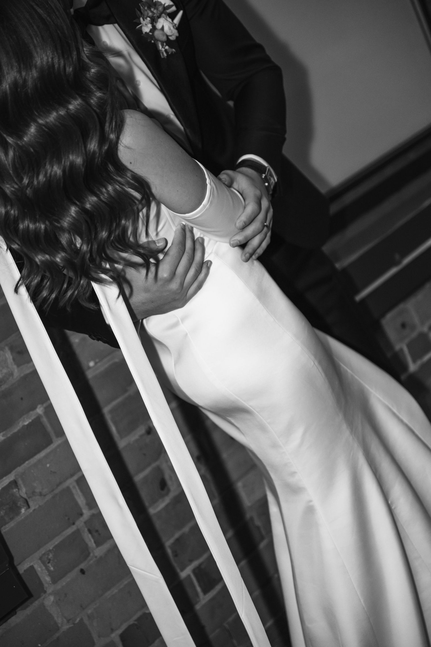 Black and white artistic photo showing detail of a silk wedding dress and hands.