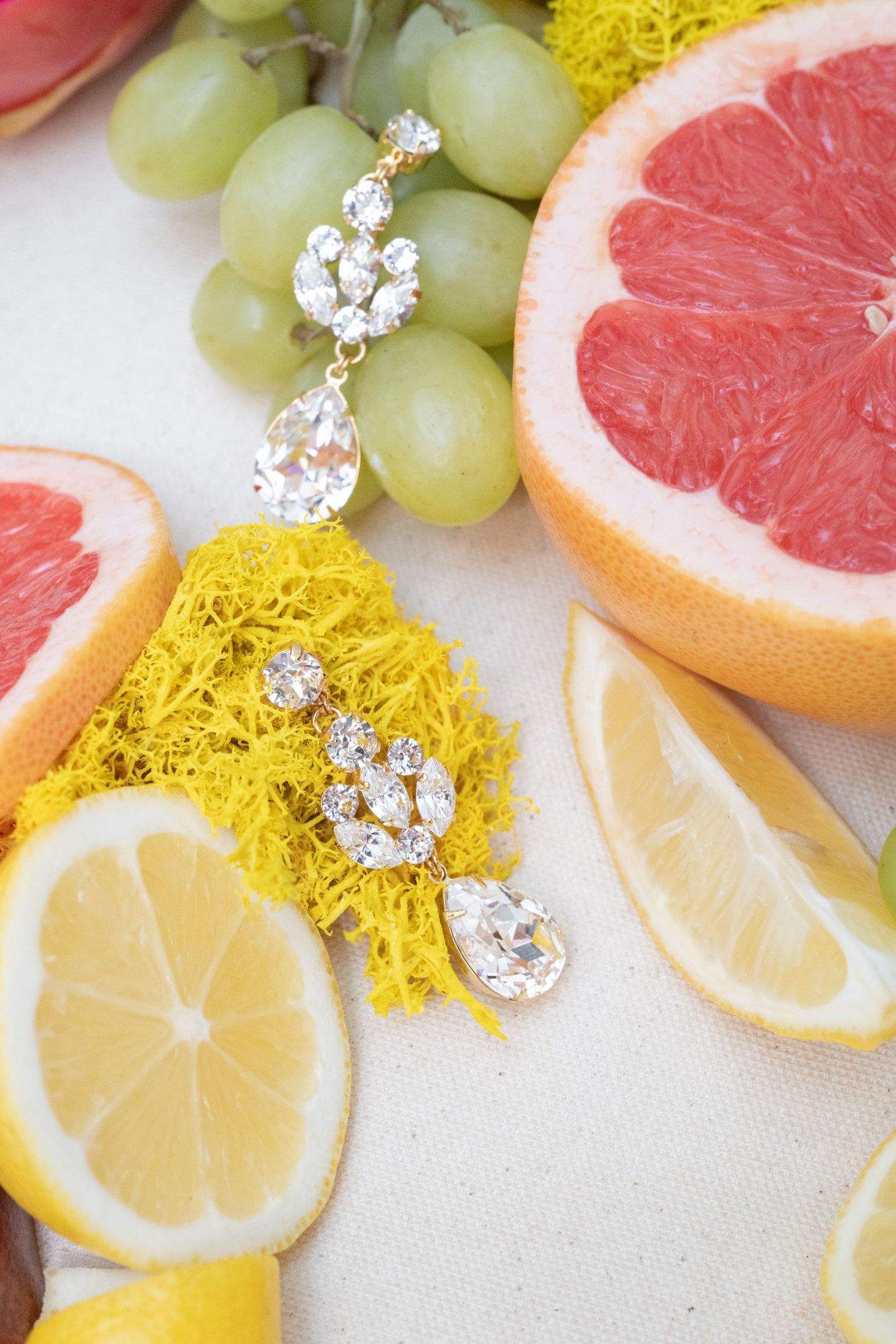 Crystal drop earring with citrus fruits and green grapes styled on white background.