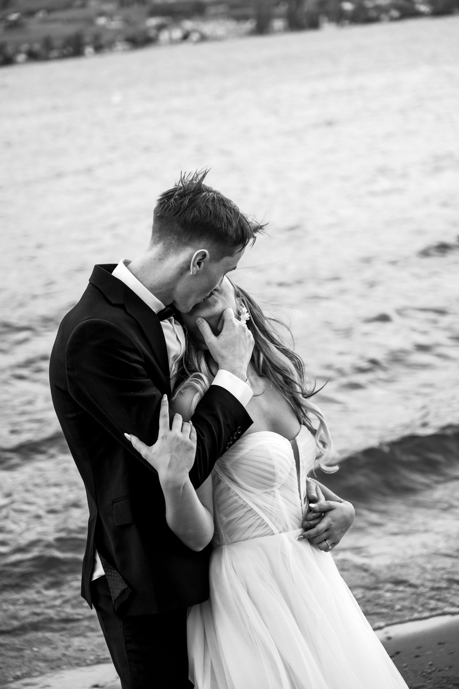 A romantic black and white wedding photo of a couple embracing by the water.