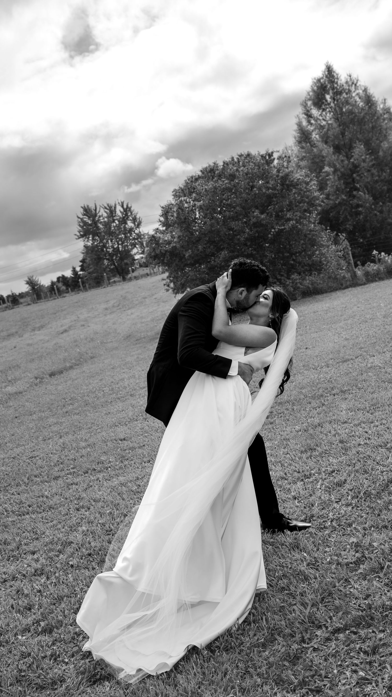 Romantic black and white wedding photo of couple embracing on grassy hillside.