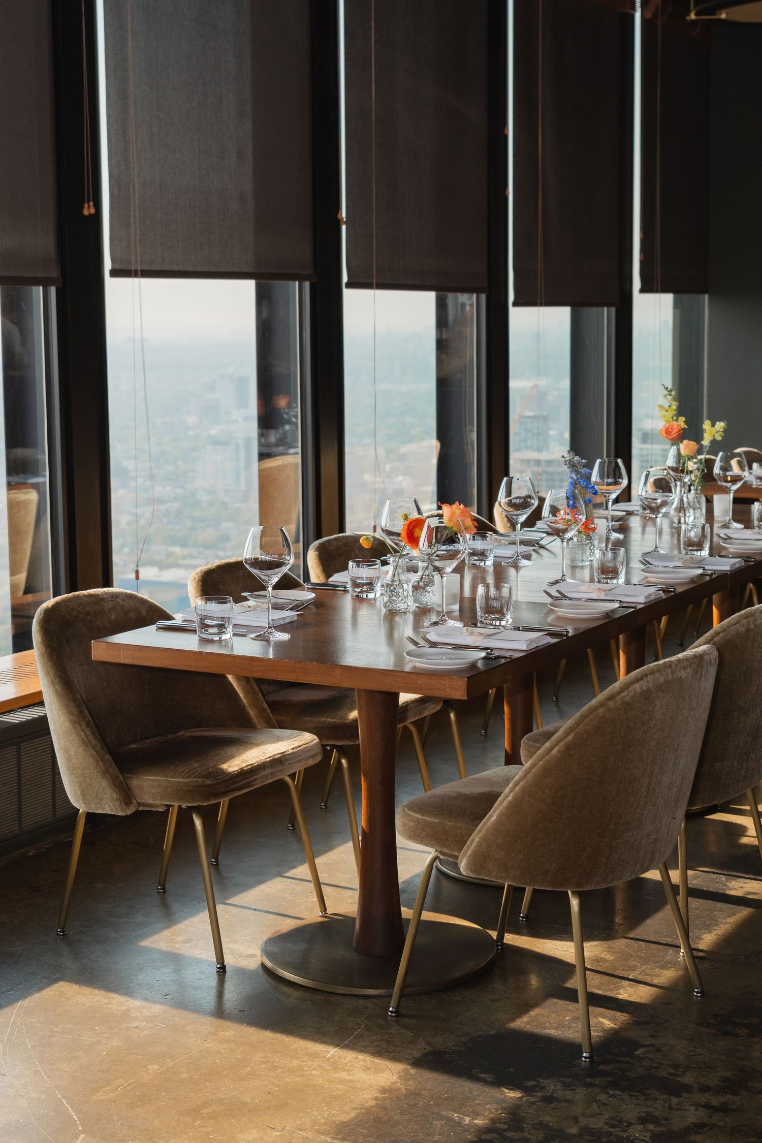 An elegant dining table set with wine glasses and place settings beside floor-to-ceiling windows in an upscale restaurant.