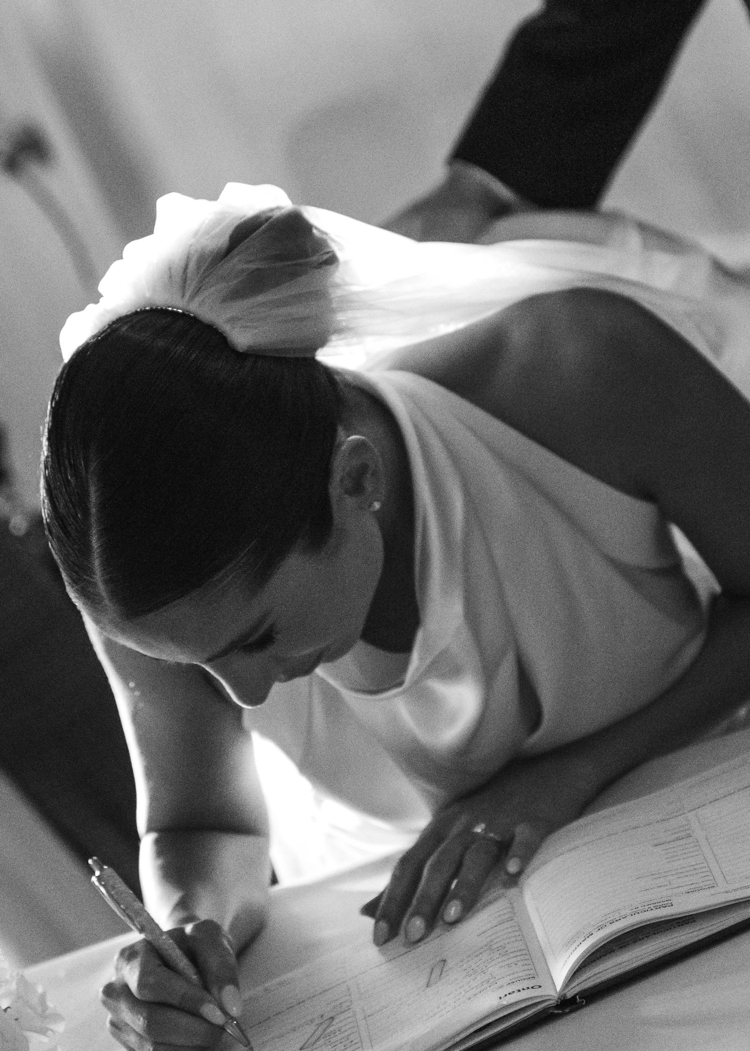 Bride in white dress signing marriage documents in black and white.