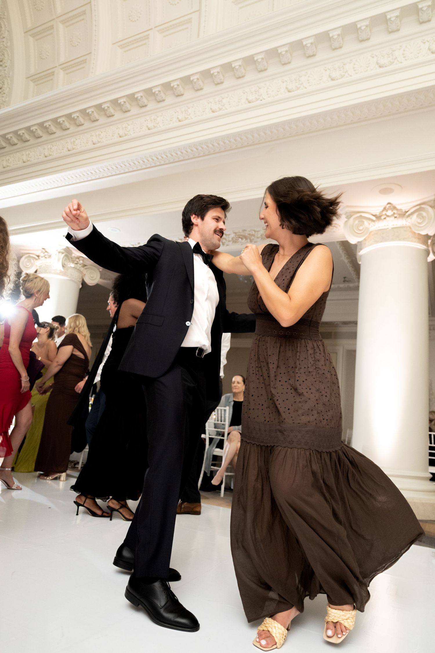 Joyful couple dancing energetically at elegant wedding reception in ornate white ballroom.