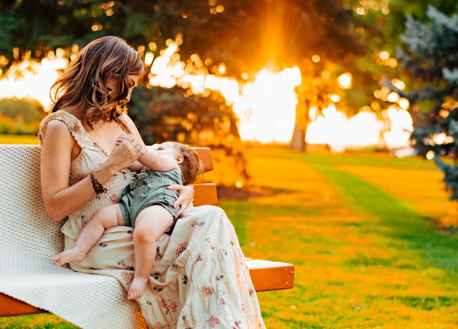 Mother breastfeeding her 6 month old baby on a bench at Sterne Park , Littleton CO. The background is a grassy land with