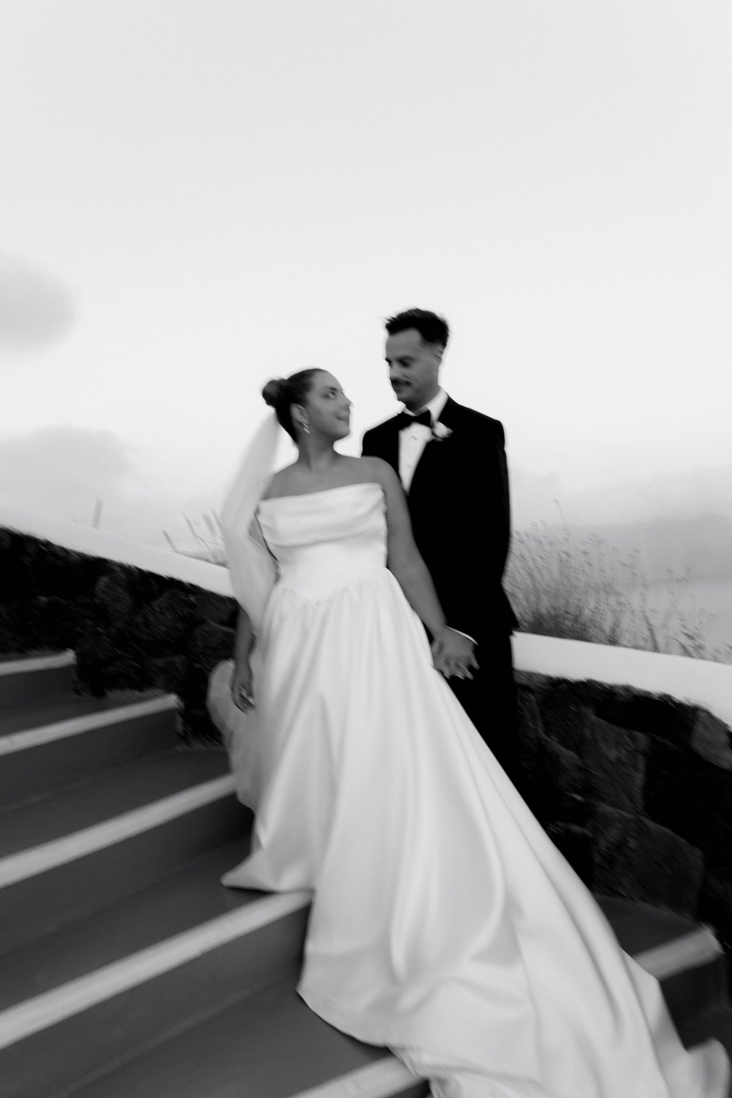 A black and white wedding photo shows a couple on outdoor steps with the bride wearing an elegant strapless gown.