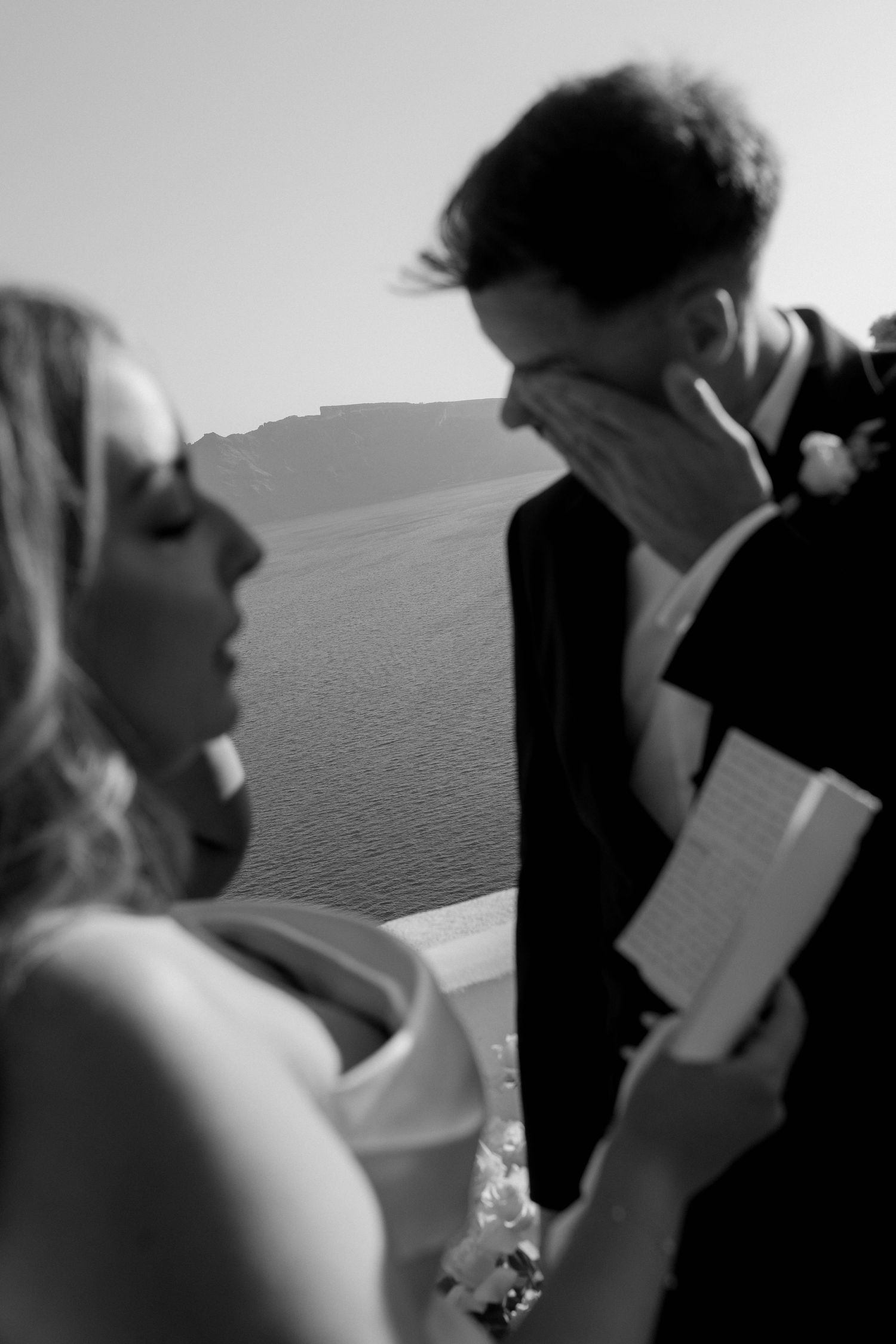 Black and white candid emotional moment between couple during wedding ceremony as bride reads vows from paper.