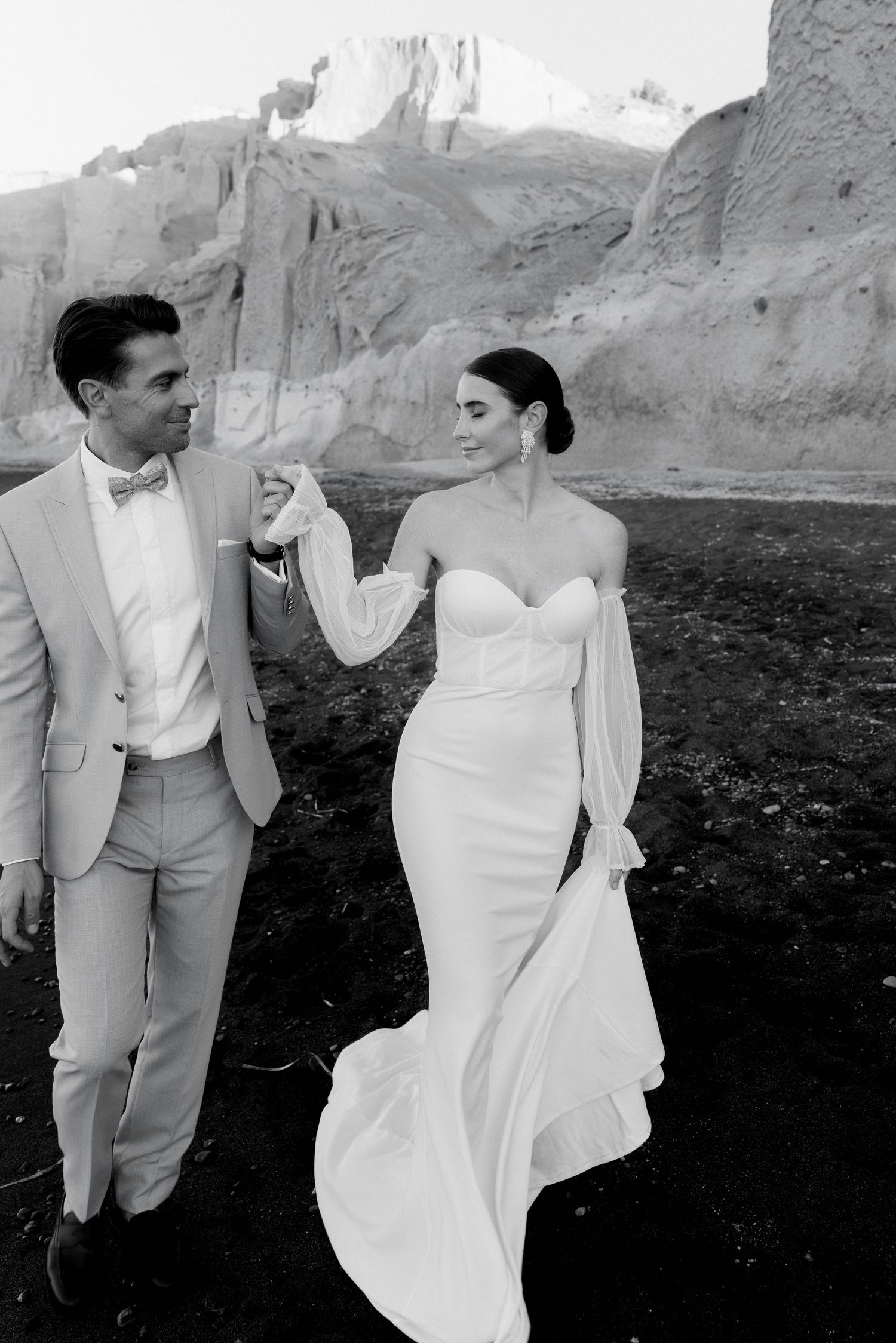 Black and white wedding photo of a couple holding hands in front of desert rock formations.
